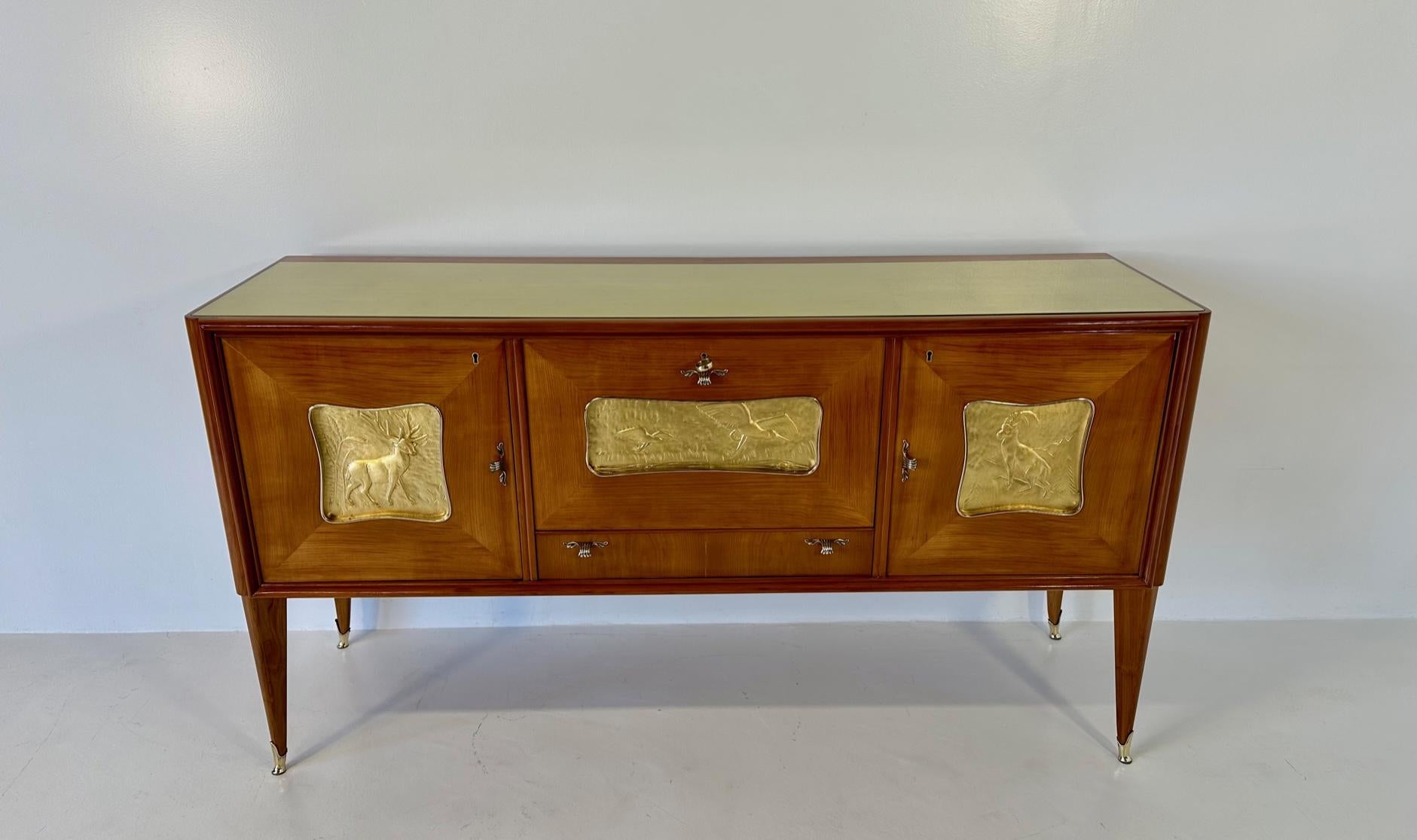 This sideboard was produced in Italy in the 1940s.
It is completely made of cherry wood with three decorations depicting animals in carved solid wood and covered in gold leaf. 
In the central door there is a dry bar. 
The details and the tips are