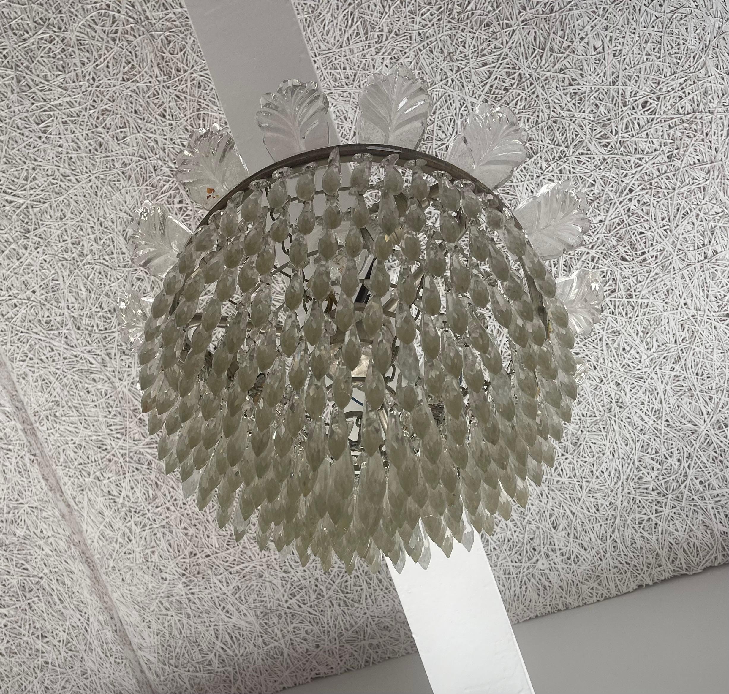 There are in fact more than a 100 prisms meticulously installed on this masterpiece of a 9 tiered chandelier with 3 light-sources. Its staired Art Deco brass band is features crystal leaves around its perimeter and each arrow shaped prism is