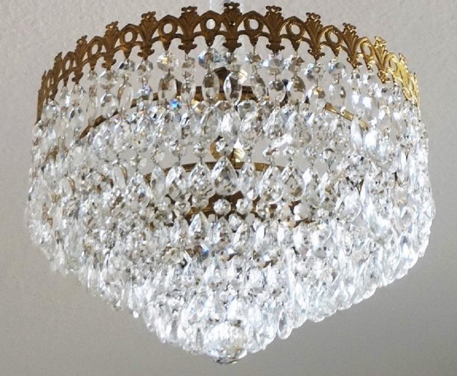 Un magnifique plafonnier Art Déco à quatre lampes en cristal en forme de cascade avec un cadre en forme de couronne en laiton doré supportant cinq étages de prismes en cristal à facettes, Italie, années 1930.
Cette pièce est en très bon état, tous