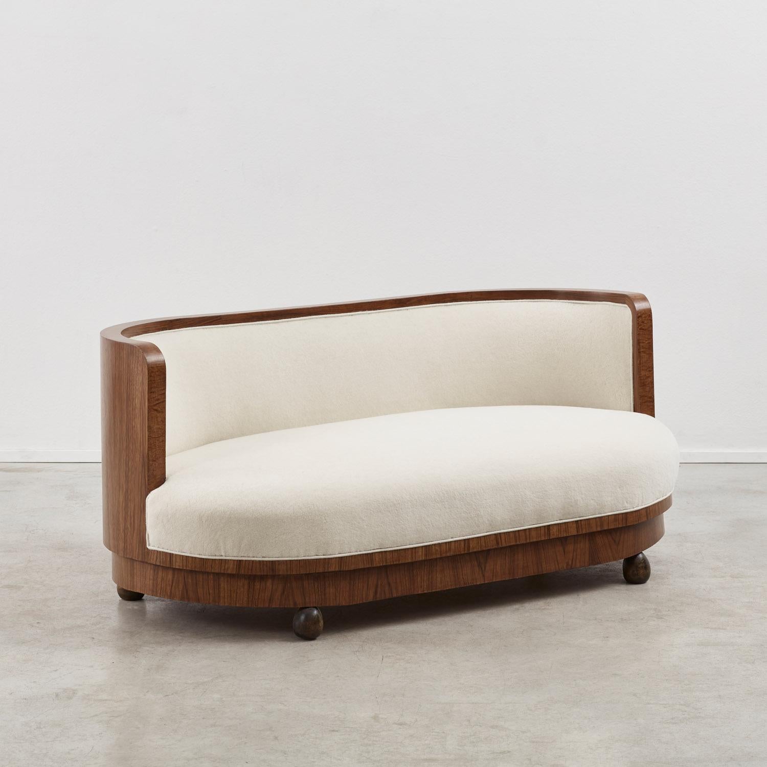 One curved, sweeping line defines this Italian Art Deco sofa. Its straight back provides architectural structure, contrasting with the plush, cloud-like seat cushioning. The sofa is finished with spherical wooden feet and a tiered base – details