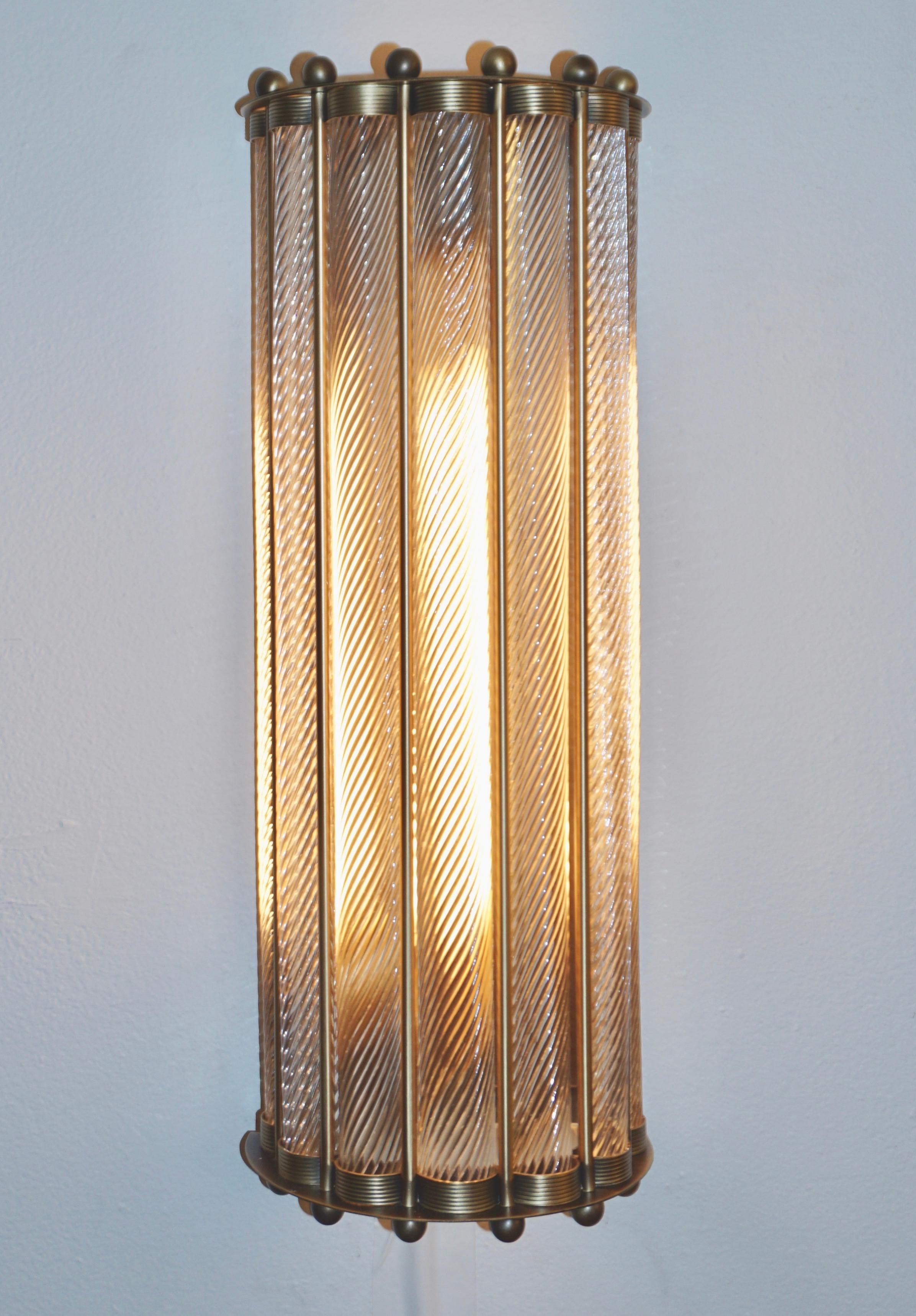 Contemporary customizable Italian Art Deco Design semi-circular wall light, entirely handcrafted, with an antique bronze finish. The nicely scalloped airy brass structure supports crystal clear Murano glass rods worked with the sophisticated