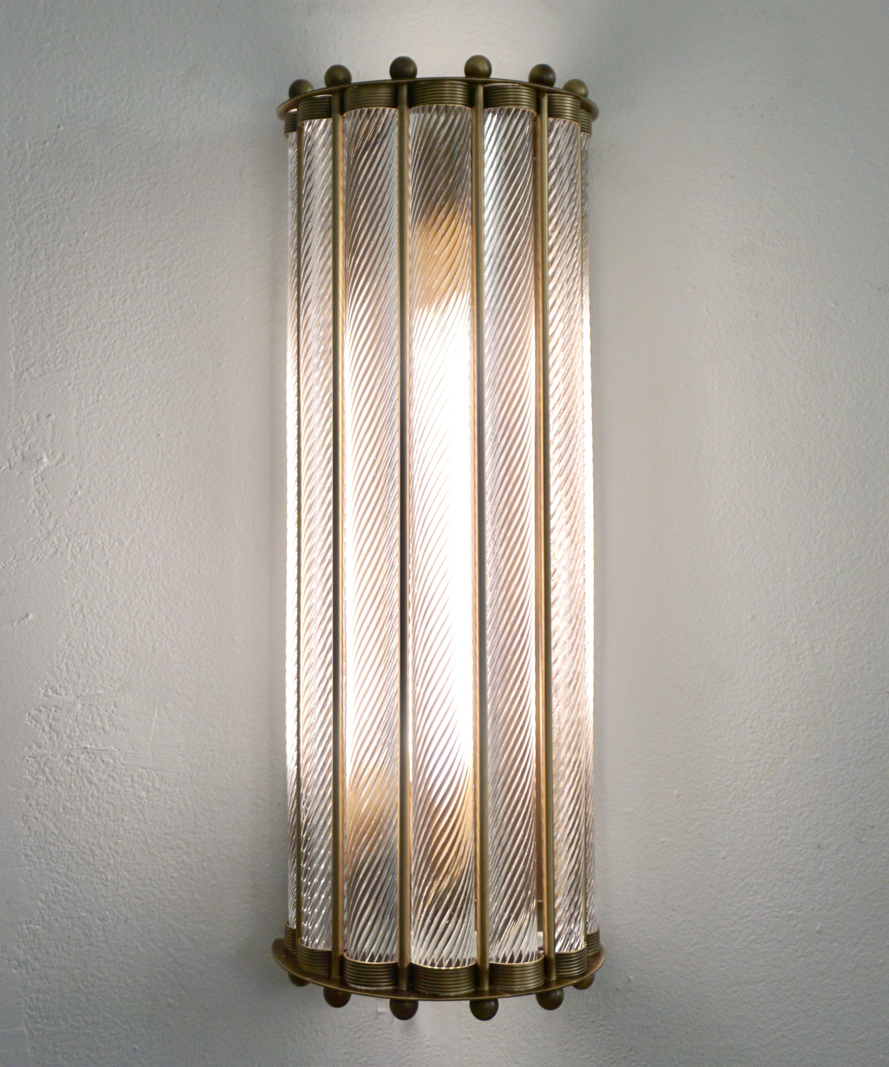 Pareja de apliques de pared semicirculares de diseño Art Déco italiano, totalmente artesanales, con acabado en bronce envejecido. La airosa estructura de latón, agradablemente festoneada, soporta varillas de cristal de Murano transparente trabajadas