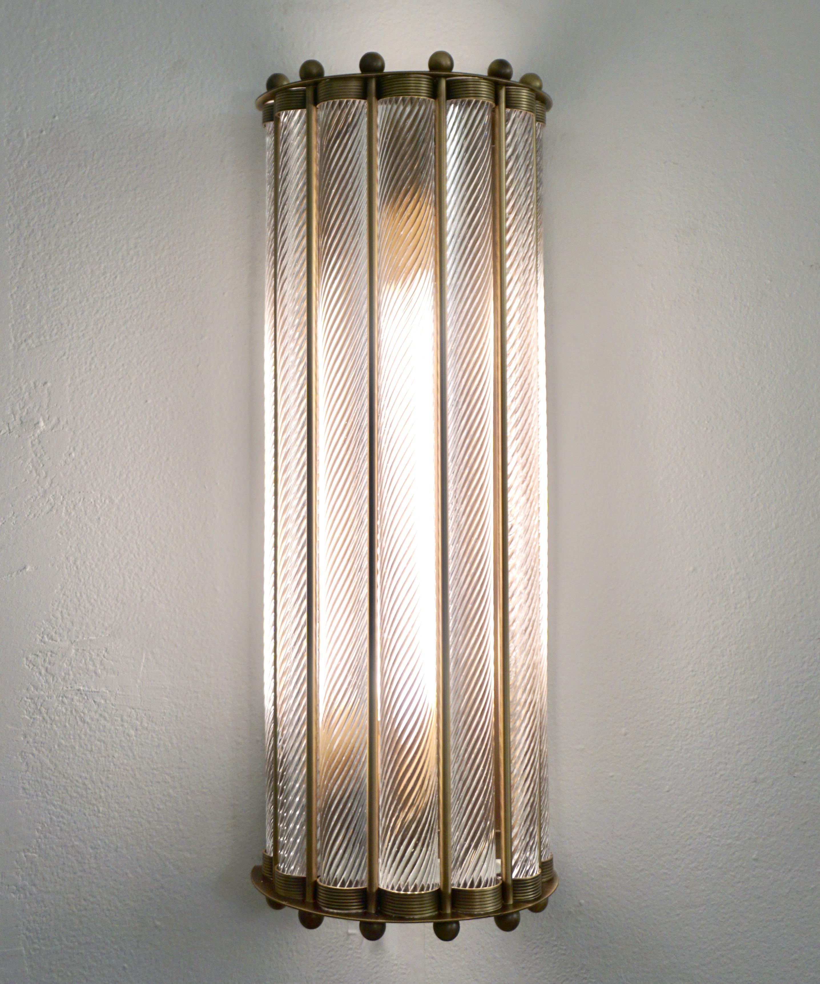 Contemporary customizable Italian Art Deco Design pair of semi circular wall lights, entirely handcrafted, with an antique bronze finish. The nicely scalloped airy brass structure supports crystal clear Murano glass rods worked with the