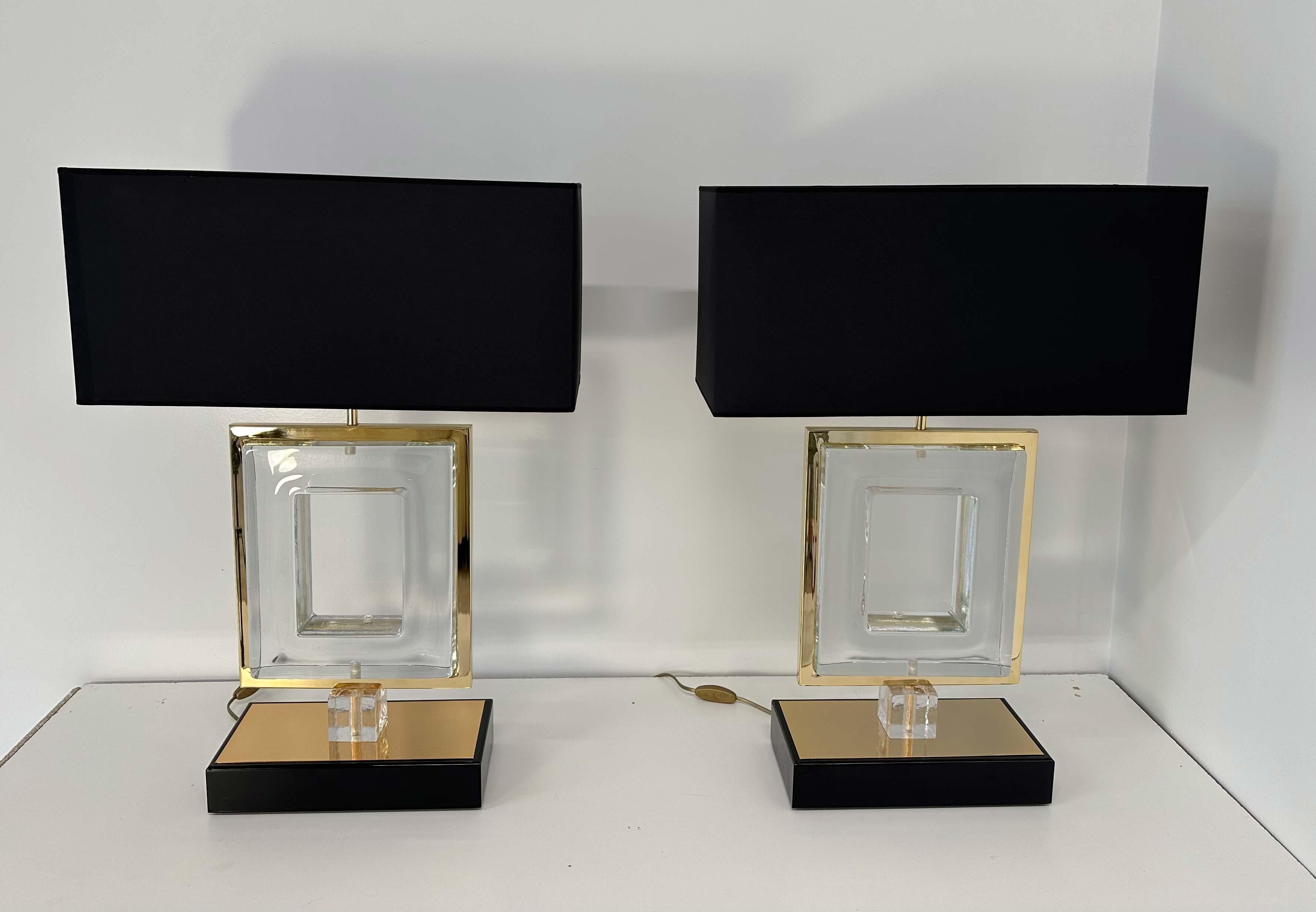 Art Deco pair of lamps, produced in Italy, more precisely in Murano, which is the world's capital for glass crafting and making. 
They are made of clear Murano glass and gold colored metal. The lampshade and the profile of the base are black. 
