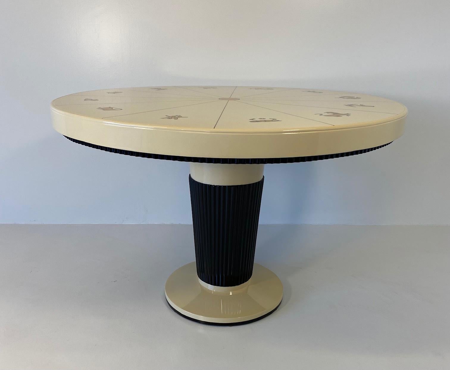 This unique table was produced in Italy in the late 1940s. 
It is completely cream lacquered with amazingly hand-made decorations in gold leaf, representing the 12 zodiac signs. The base and the profiles are black lacquered. This design clearly