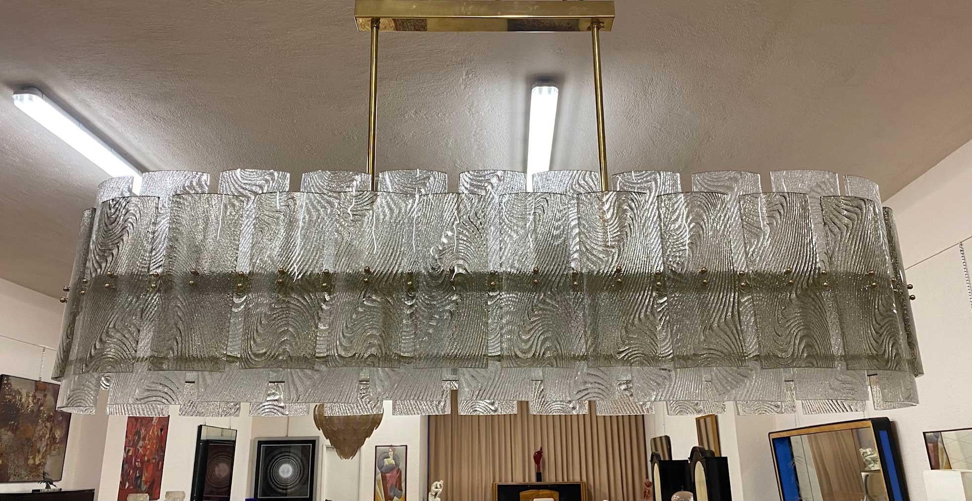 Murano glass chandelier composed of 48 rectangular pieces of clear glass and 48 smaller rectangles of grey glass. All have a particular decoration in their inner part and are placed on an oval-shaped brass structure. The underside is frosted glass.