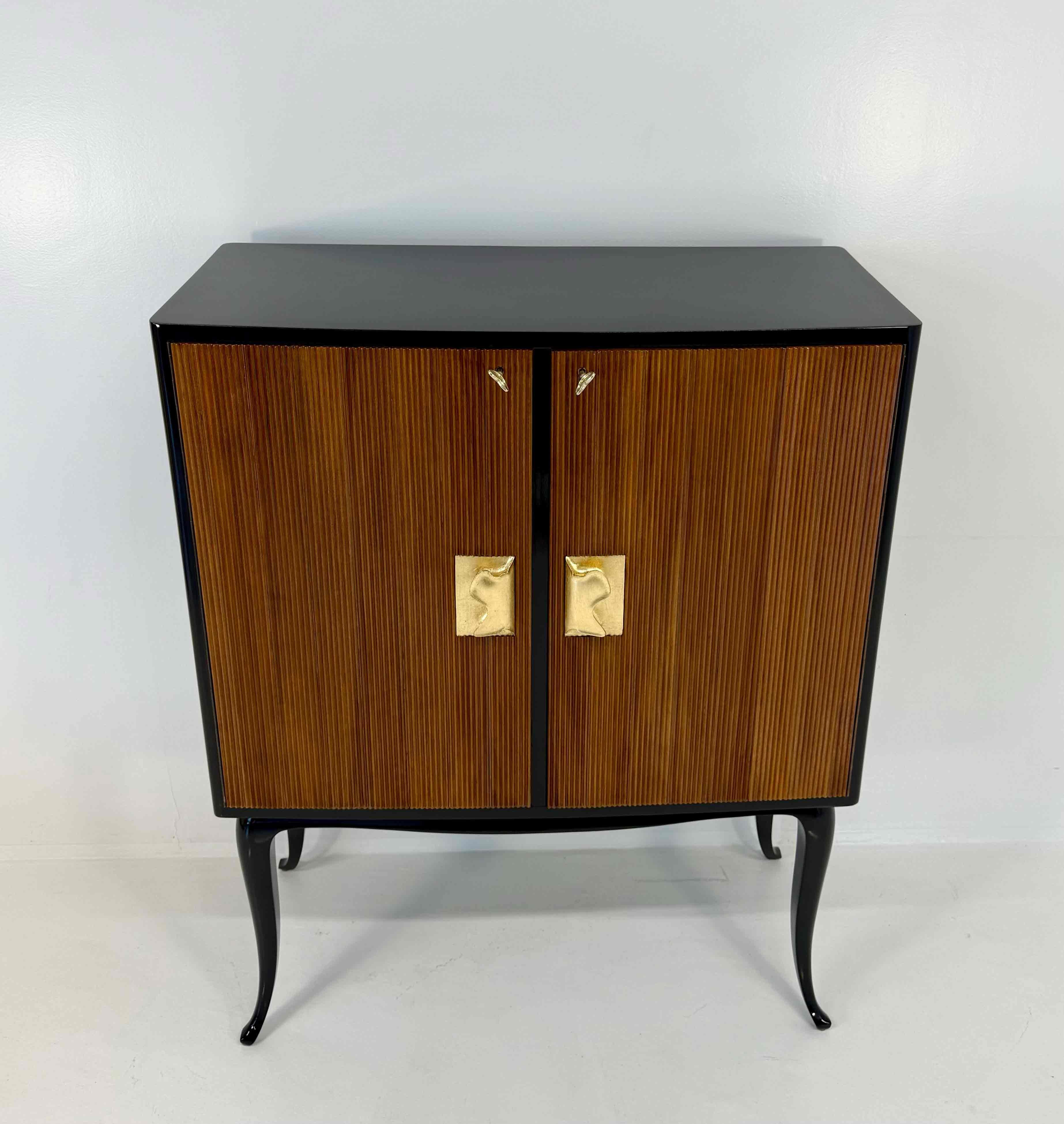 Refined Italian bar cabinet from the 1950s, attributed to Osvaldo Borsani. The structure is entirely finished in glossy black lacquer, featuring elegant front doors in fluted walnut that add rhythm and depth to the design. The finely carved handles,