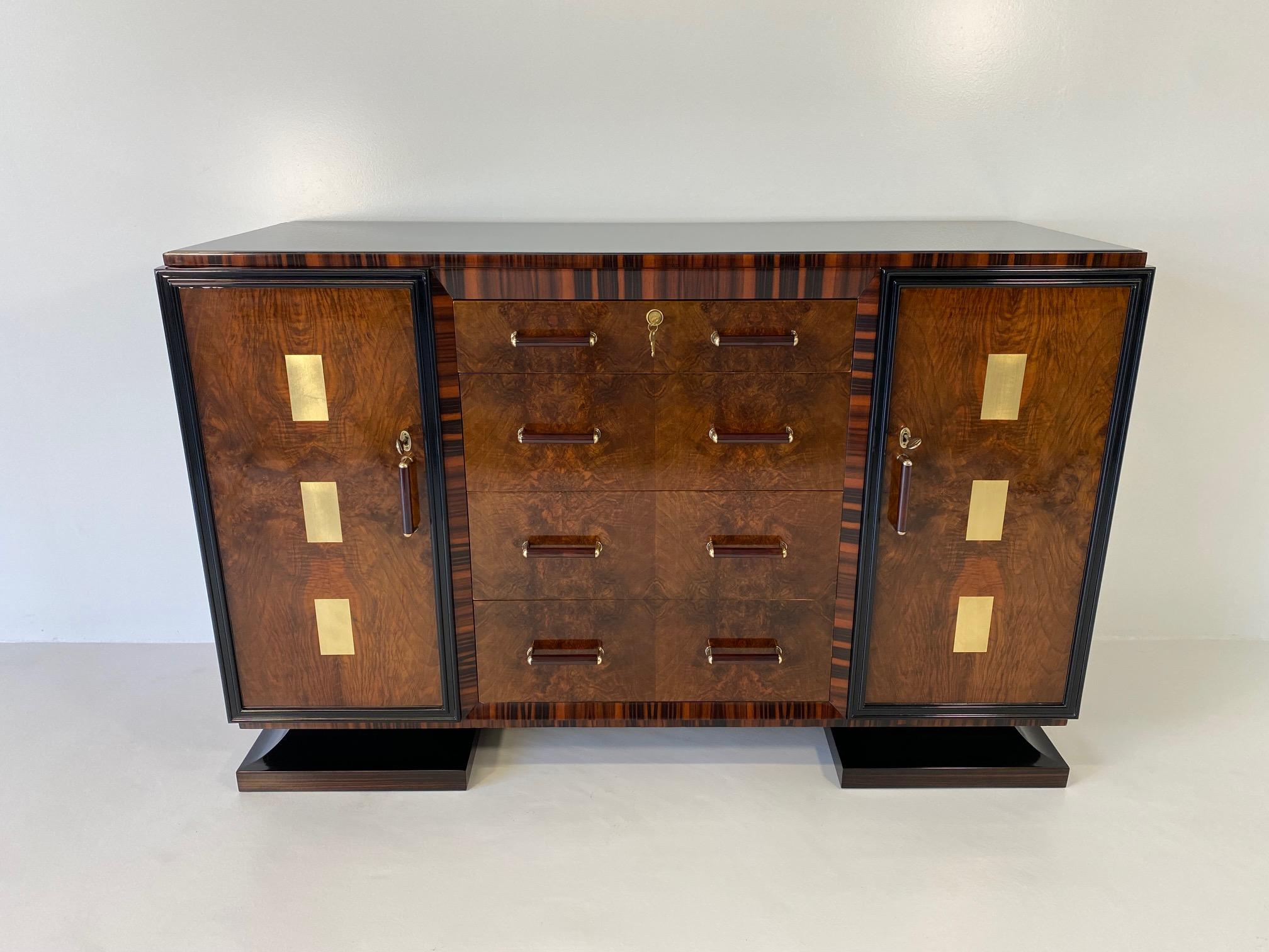 This Art Deco sideboard was produced in Italy in the 1940s. 
It features two different wood essences; walnut briar and Macassar, framed by black lacquered profiles. There are four drawers and two doors, on which there are gold leaf decorations.