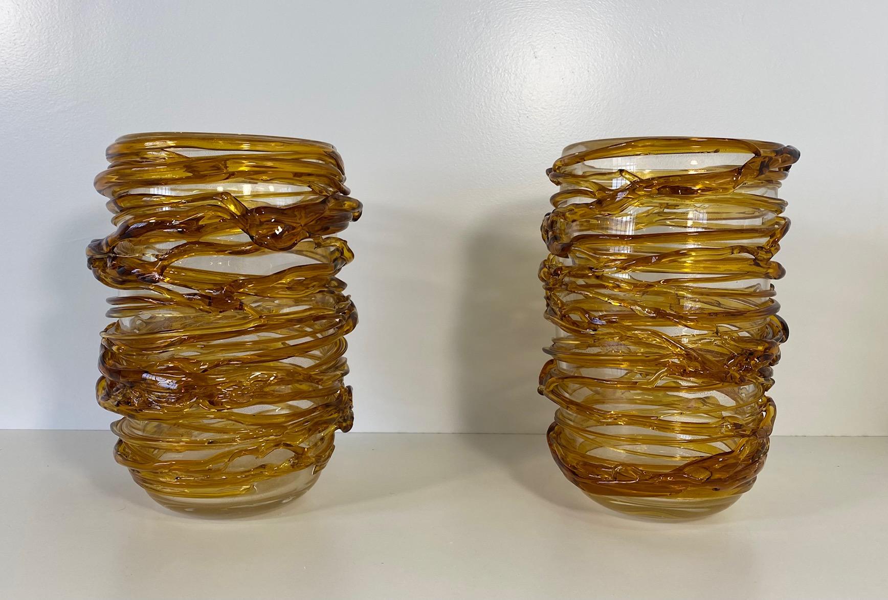 This unique pair of vases was produced in Italy, more precisely in Murano, which is the world's capital of glass art making and crafting. 
They are completely made of amber colored Murano glass, which has been particularly and finely crafted to