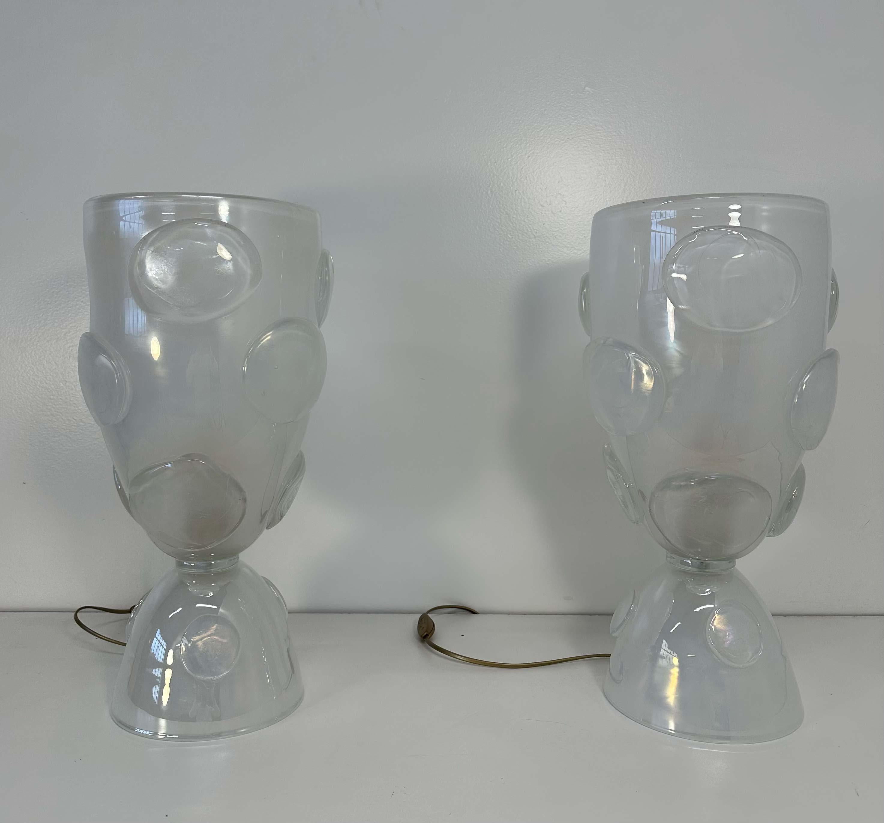 This pair of vase lamps was produced in Italy, in Murano the world's capital of glass making. 
They are completely made of white Murano glass, with decorative circles are made of the same particular Murano glass.

    
