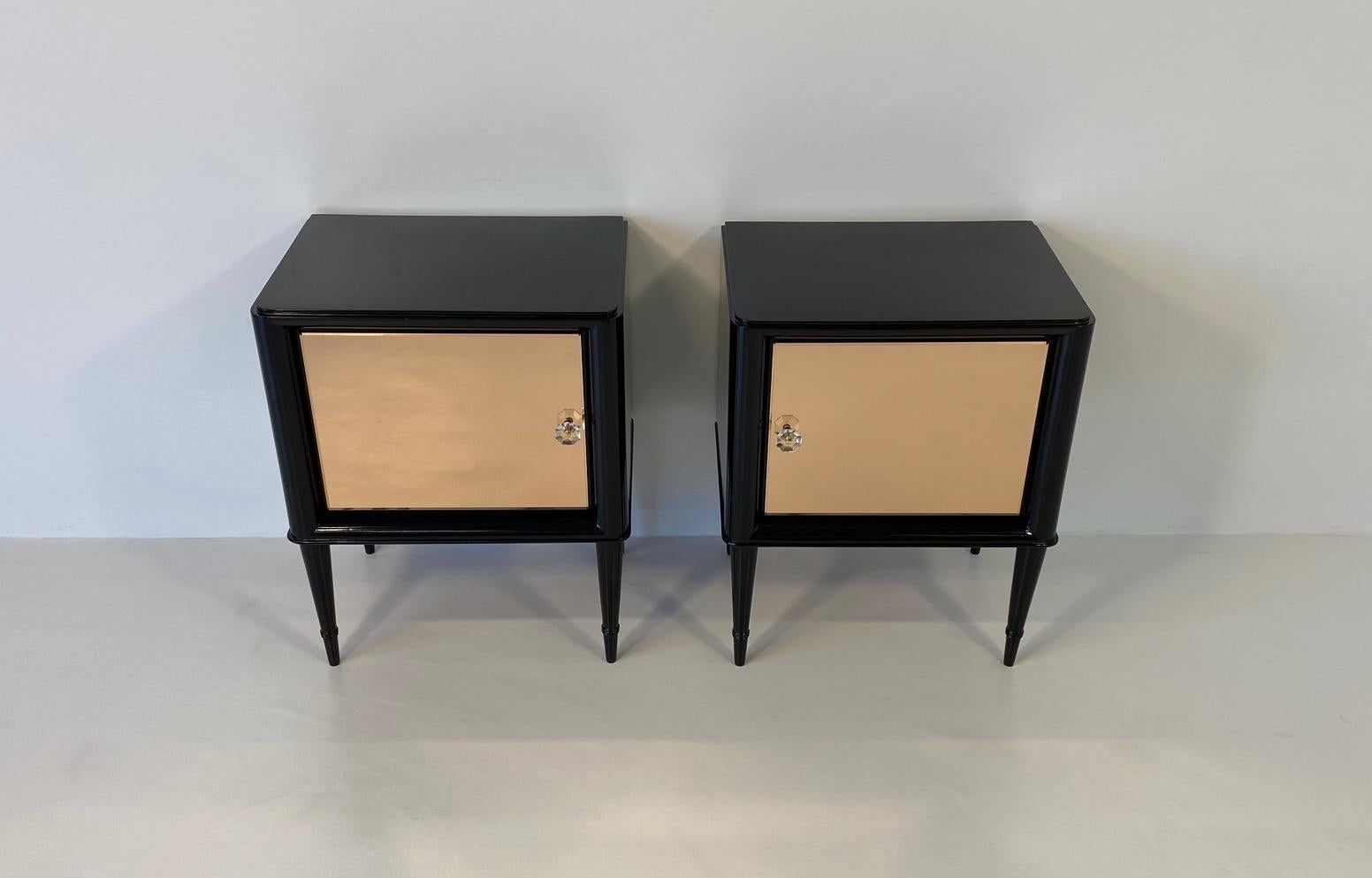 This elegant yet particular pair of nightstands was produced in Italy in the 1950s. 
They are completely black lacquered with rose mirror doors. 
They have been completely and finely restored.