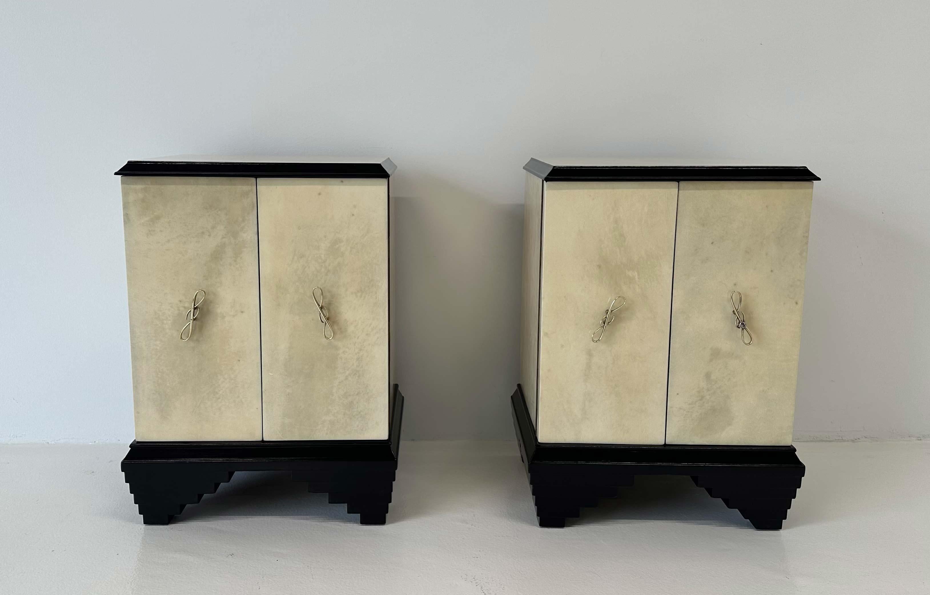 This pair of Art Deco nightstands was produced in Italy in the 1930s. They are completely covered with parchment, with black lacquered profiles of the top and base. The handles are in brass. 
There are two doors on the outside and a drawer on the