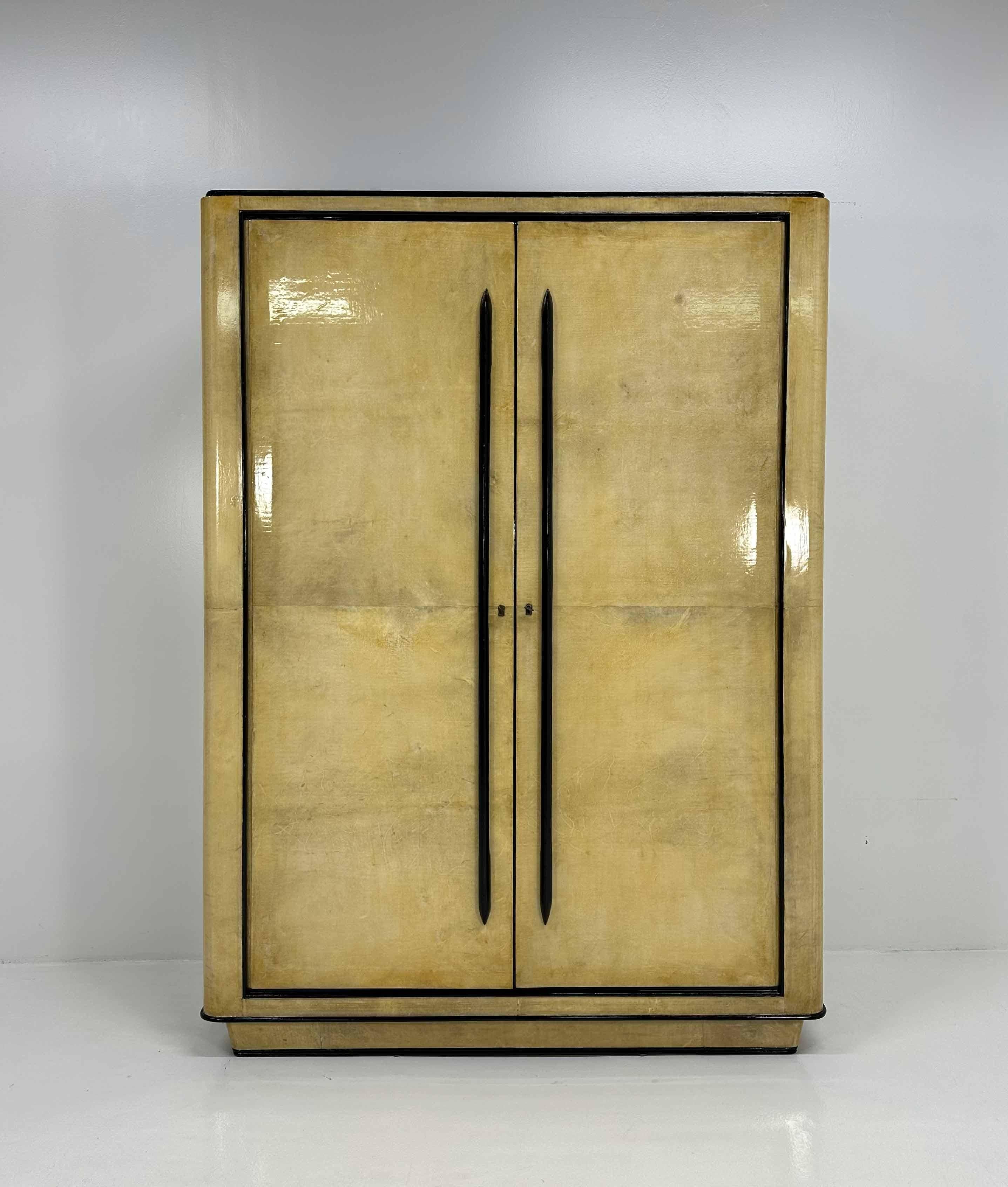 This stunning Art Deco Armoire was produced in Italy and it is attributable to Guglielmo Ulrich. 
It is completely covered in Parchment (goat skin) and has details, such as the handles and the profiles, walnut dyed. 
On the interiors there is a wide