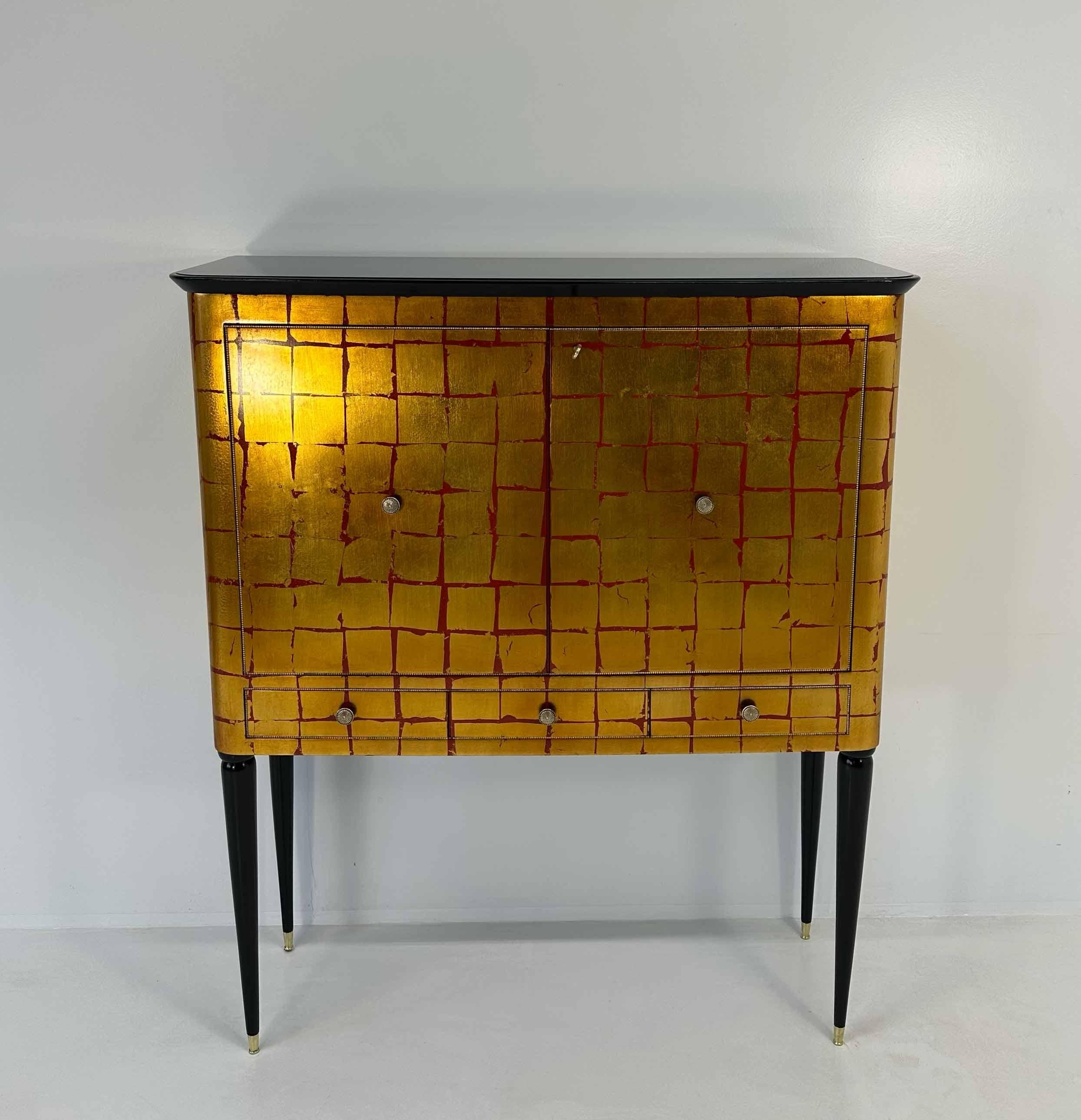 Ce meuble de bar particulier et rare a été produit dans les années 1950 en Italie.
Il est entièrement laqué rouge avec un décor à la feuille d'or qui rend ce meuble unique.
Les profils et le plateau en verre sont noirs tandis que les poignées et les
