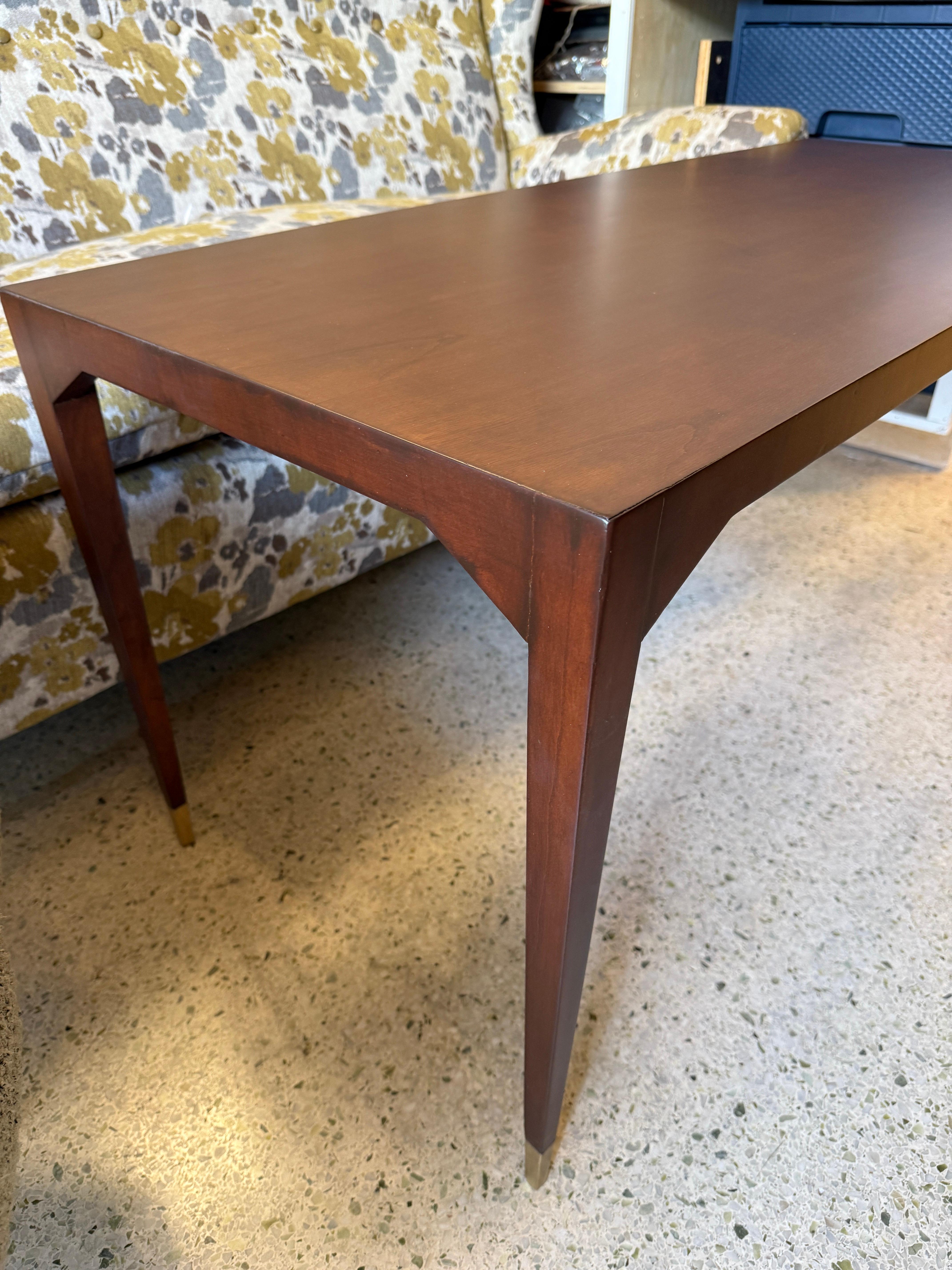 Cette magnifique table de cocktail en bois et laiton présente un plateau et des pieds en bois riche dans le ton de l'érable foncé et finis avec d'élégants sabots en laiton.  La finition satinée du bois rend cette table prête à être placée dans votre