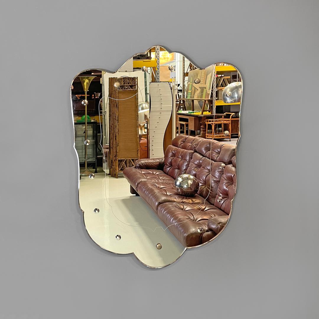 Italian Art Deco shield-shaped wall mirror with round decorations, 1940s
Shield-shaped wall mirror. The mirror has contoured profiles with curved and rounded shapes. On the circumference of the mirror there are three round metal elements that join