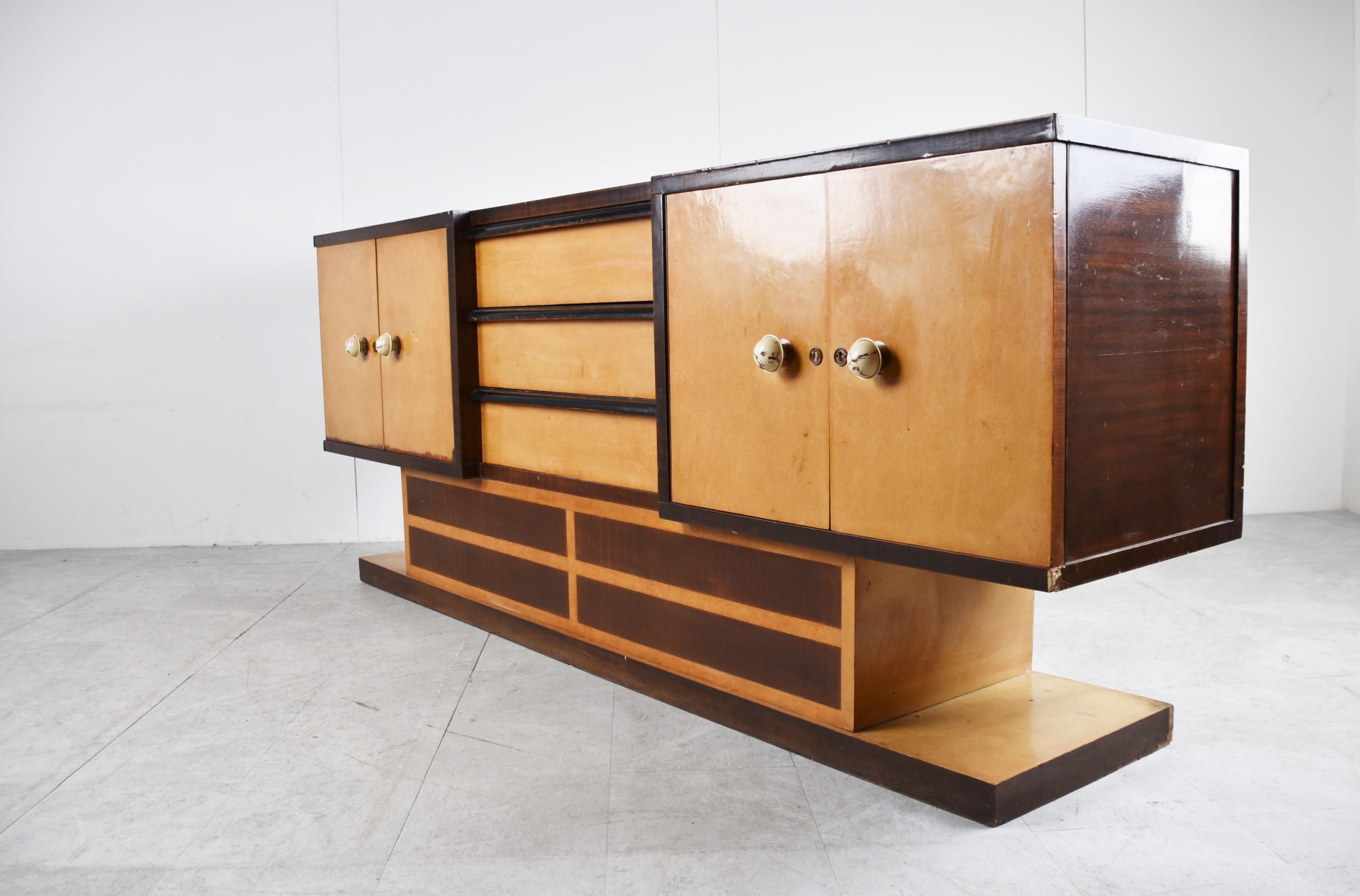 Striking two tone wood italian art deco sideboard.

The sideboard features 4 doors and three central drawers and white bakelite handles.

Beautiful art deco era design piece with beautiful colours.

Good overall condition with some age related