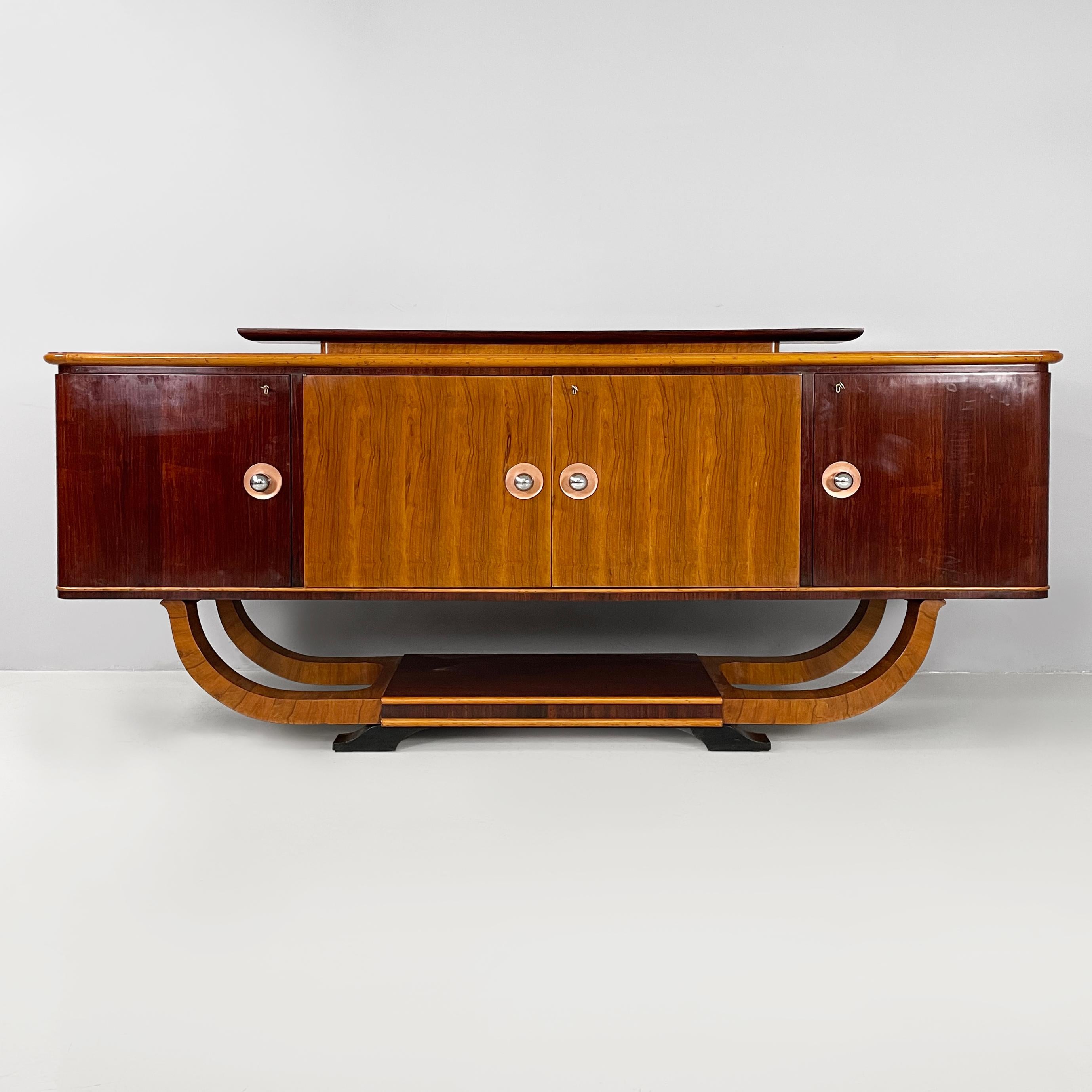 Italian Art Deco Sideboard in wood with metal handles, 1920s
Rectangular-based sideboard with rounded front corners, in light and dark wood. On the top there is a raised shelf, also with rounded corners. On the front there are three compartments. A