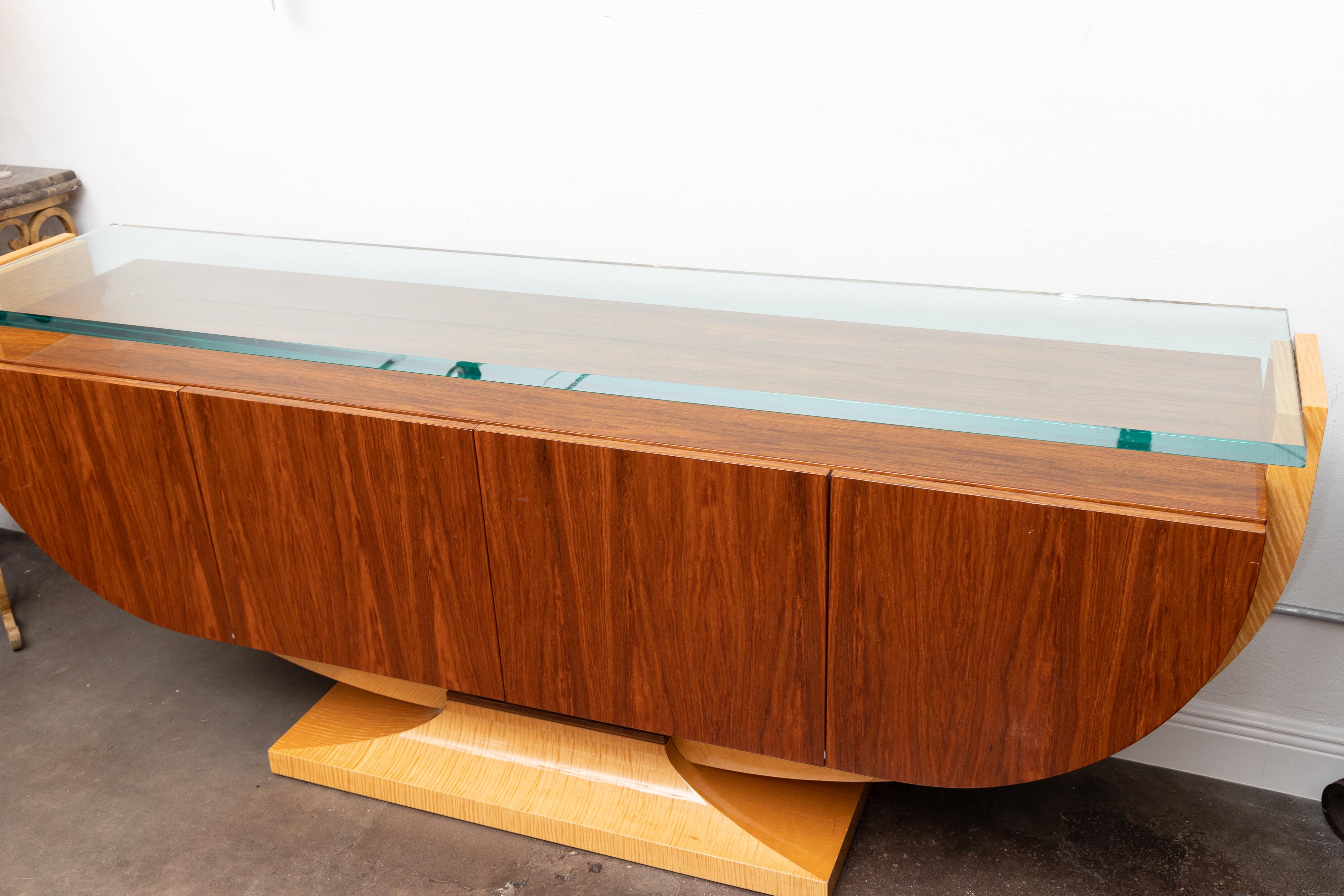 This is a graceful Italian rosewood credenza with a thick glass super structure above a rosewood top over a long cabinet with two central doors opening to reveal two banks of shelving. The cabinet section is in the shape of a demi-ellipse, situated