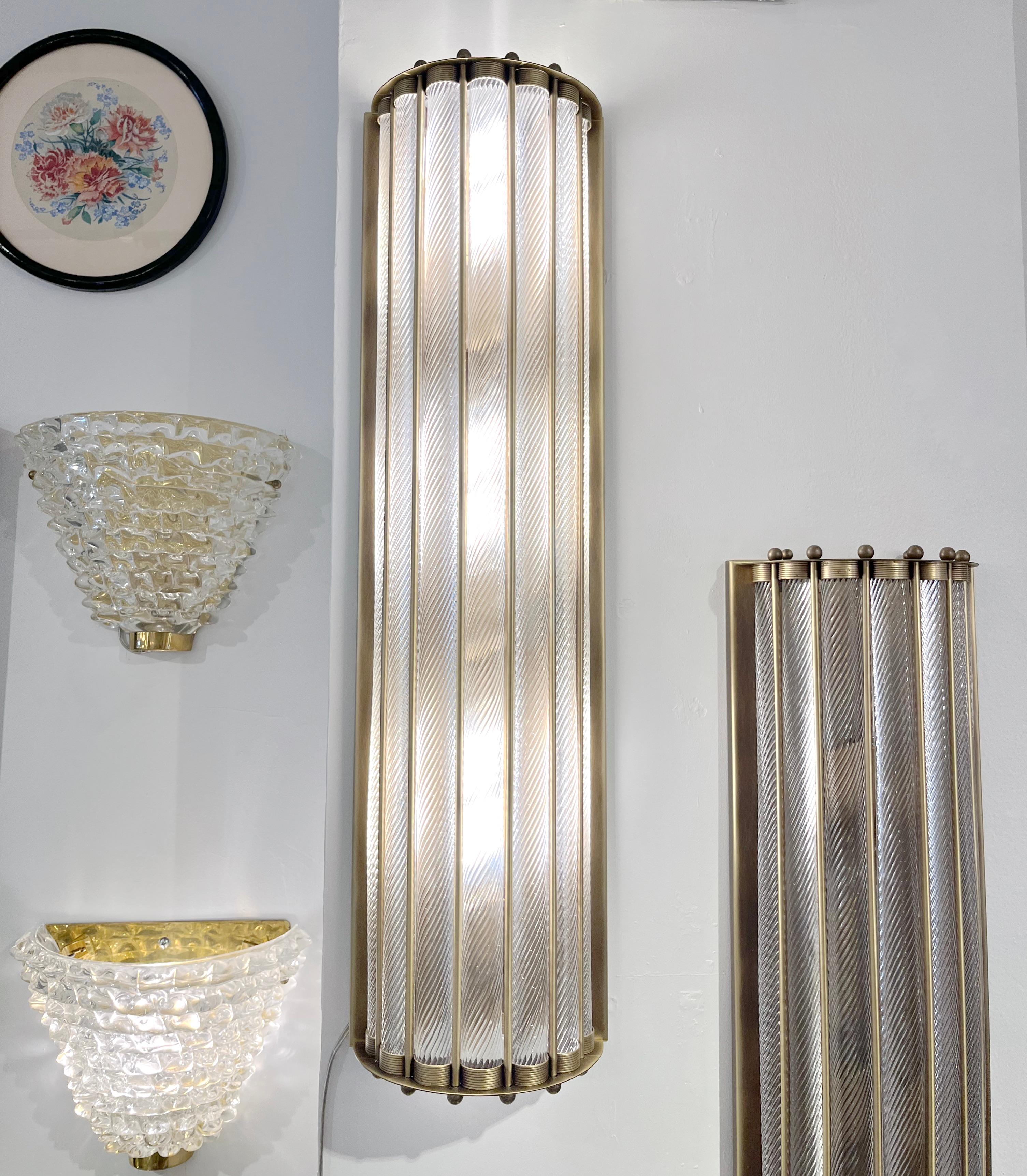 Contemporary customizable Italian Art Deco Design pair of semi-circular wall lights, entirely handcrafted in Italy, with an antique bronze finish. The nicely scalloped airy brass structure supports crystal clear Murano glass rods worked with the