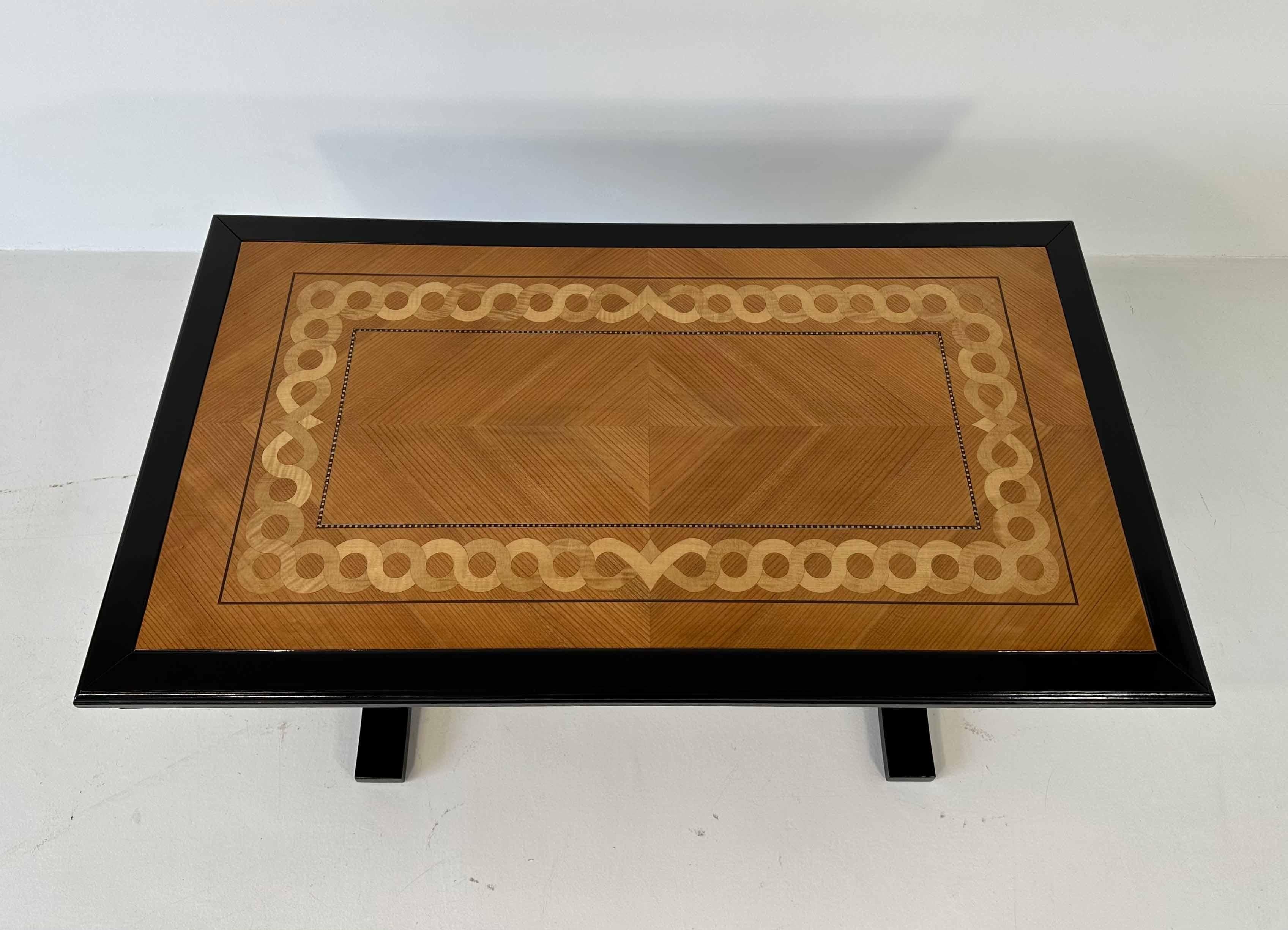 This coffee table was produced in Italy in the 1980s. 
The top is inlaid with different essences of wood, among which there are ash wood and maple. The legs and the carved lateral profiles are ebonized. 
The tube that connects the two legs is in