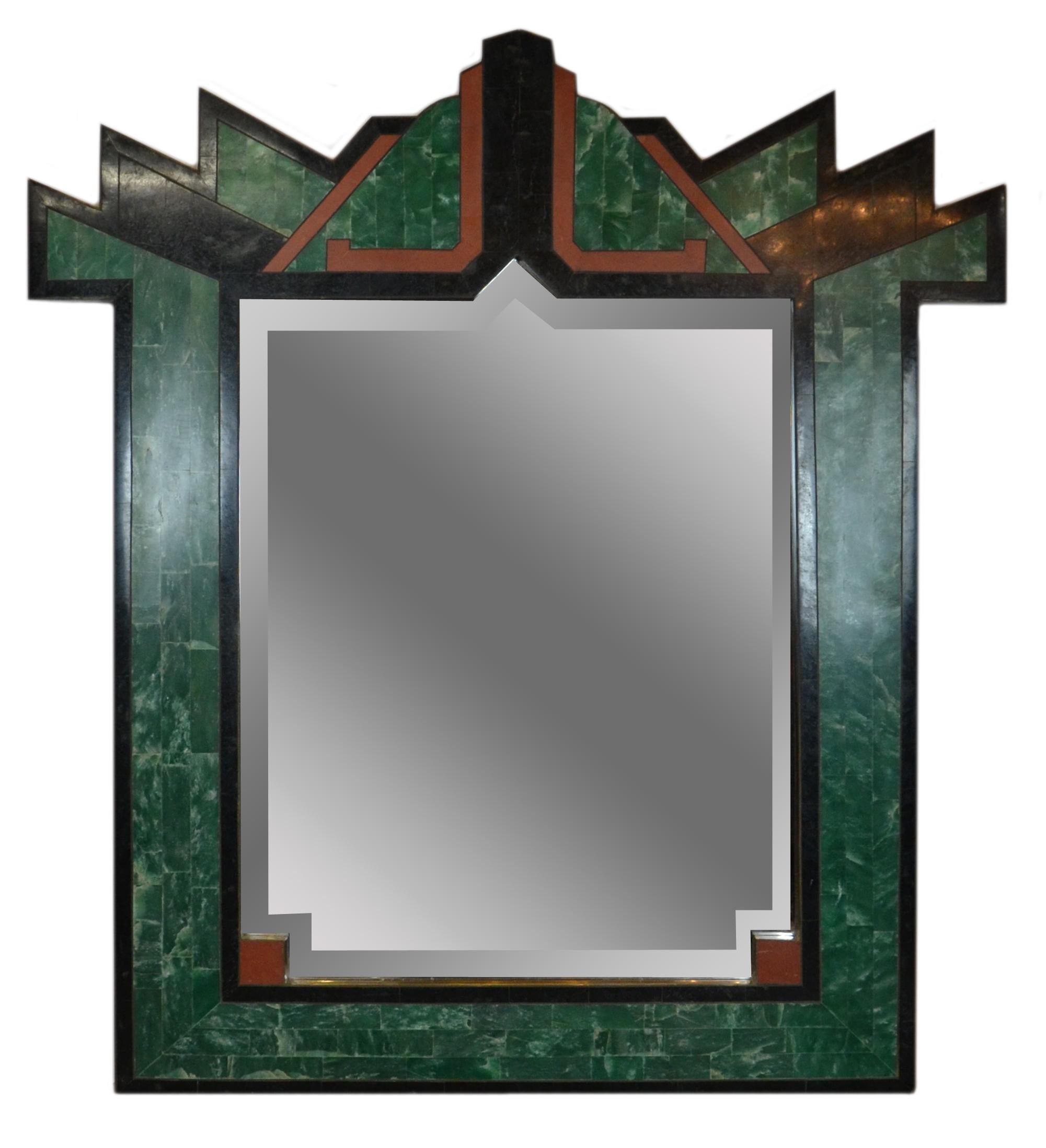 Italian Art Deco style mirror with green, black, orange-red color stones framed in solid brass. The mirror is cut in the shape of the frame with a beveled edge.
 