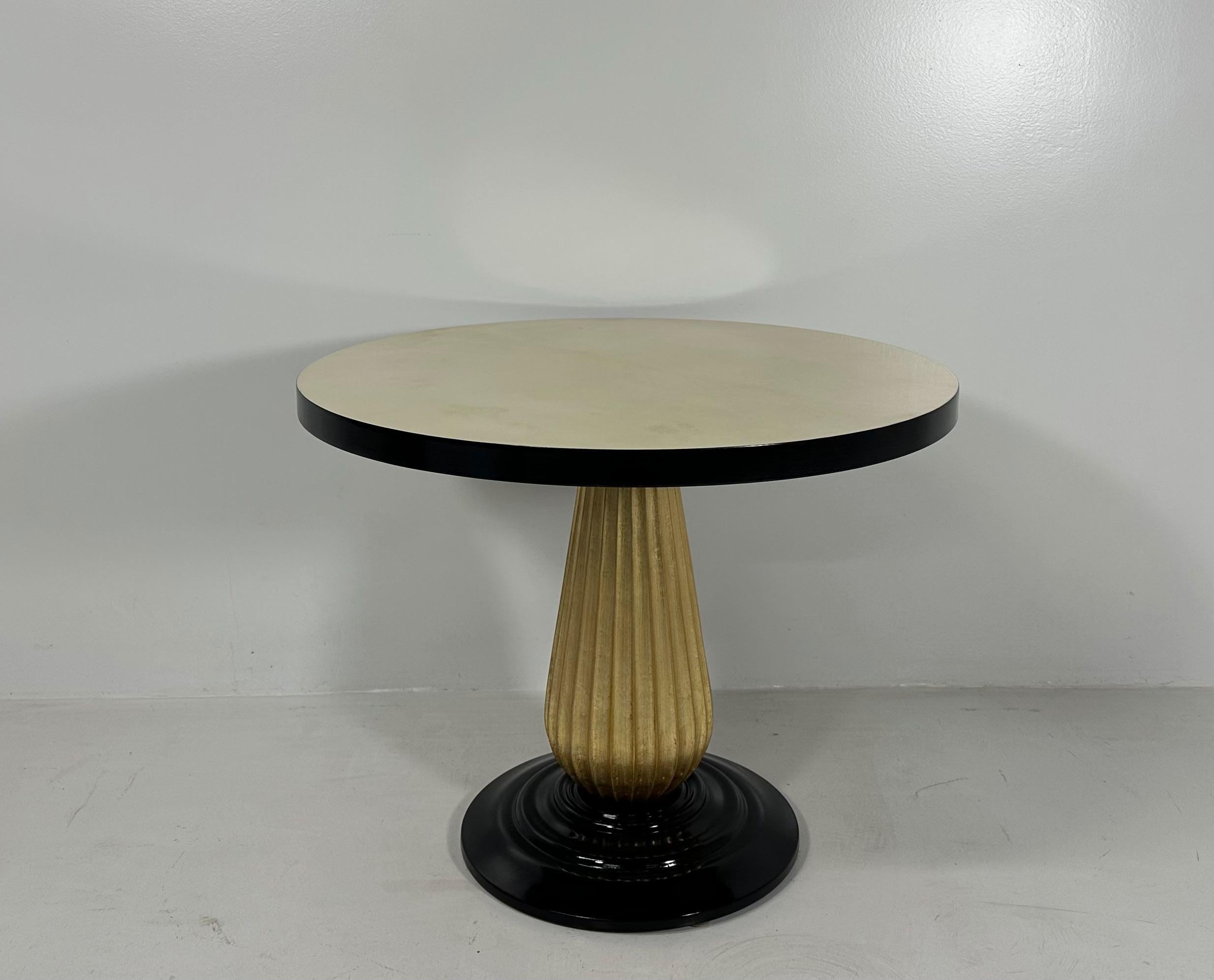 Cette table basse de style Art déco a été produite en Italie dans les années 1980. 
Le plateau est en parchemin avec un profil laqué noir, le pied tourné en colonne est en feuille d'or et la base est laquée noire.
Entièrement restauré. 