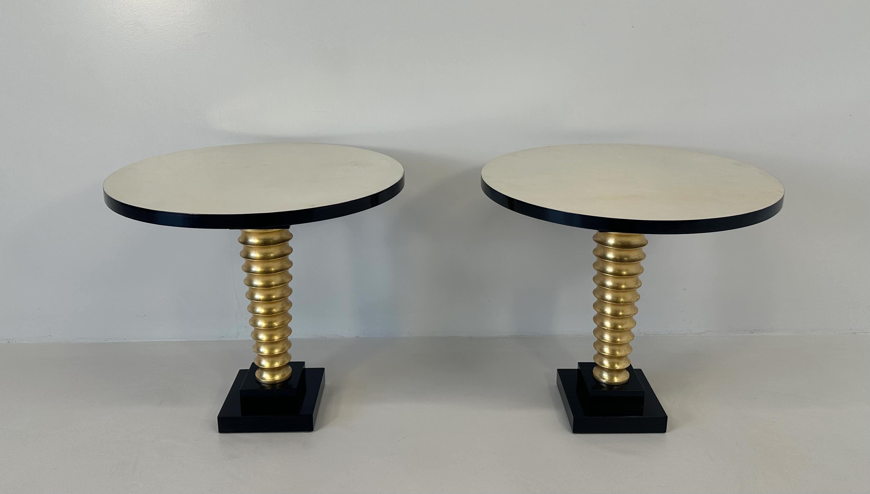 This elegant pair of Art Deco Style coffee table was produced in Italy. 
The top is in parchment, the details such as the profiles of the top and of the base are black lacquered, while the leg is in gold leafed turned wood. 
