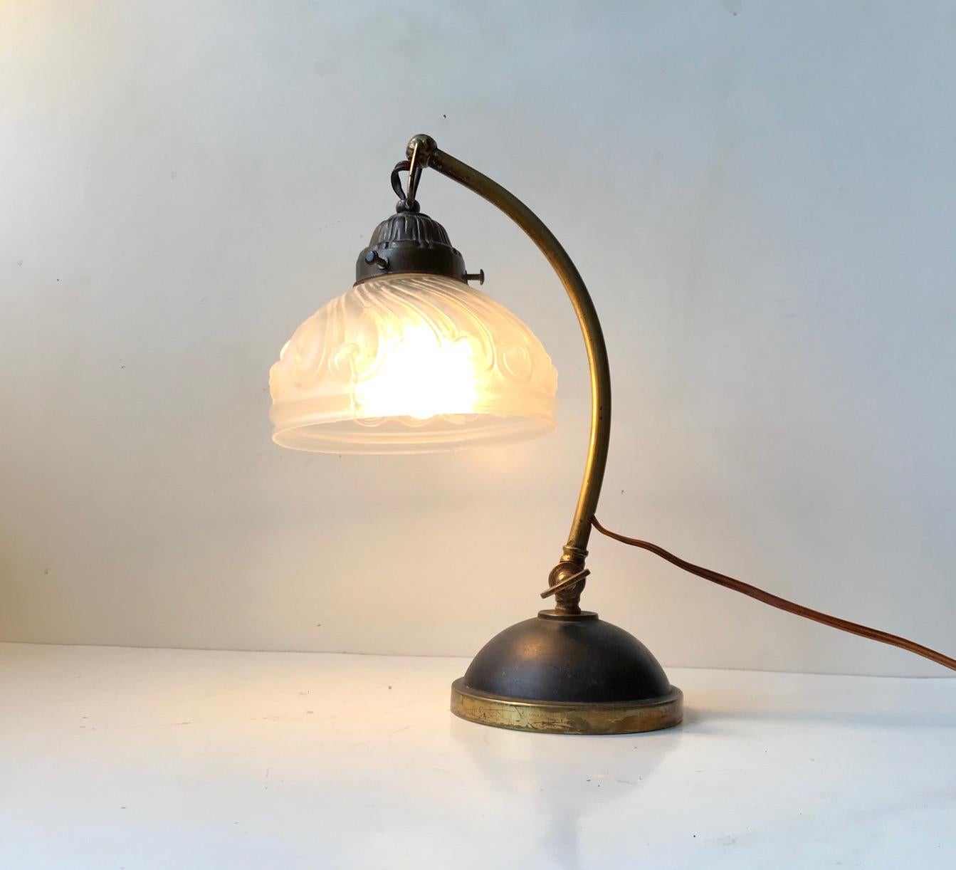 A stylish table lamp manufactured in Italy circa 1930-40. It features a swag loose hanging molded glass shade with waves, a partially patinated solid brass base and a mechanism for a adjusting the angle of the stem. Measurements: H: 30 cm, Diameter: