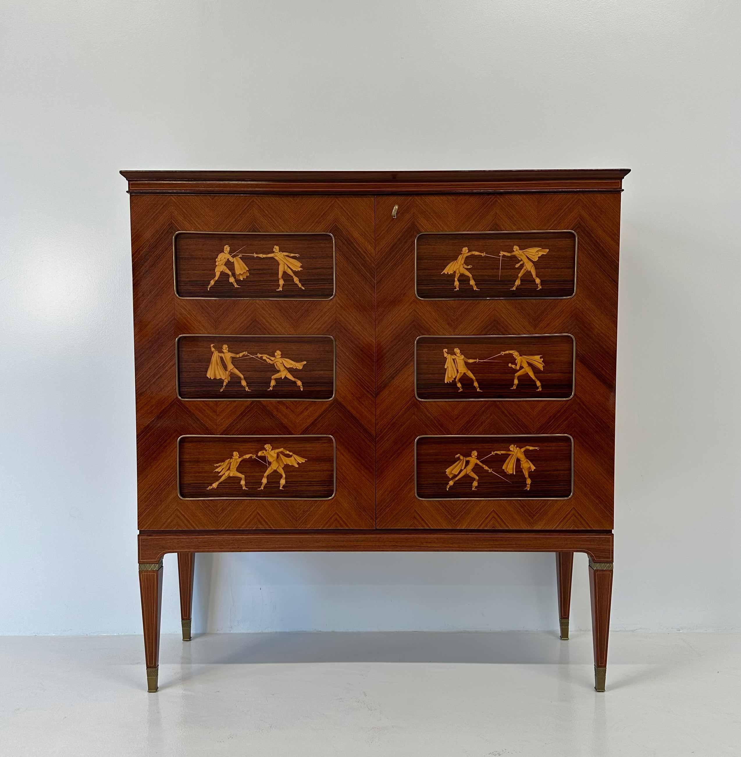 Ce meuble de bar Art déco a été produit en Italie dans les années 1950 par Paolo Buffa. Il est entièrement en bois de teck avec un motif à chevrons. Sur les portes, six panneaux décoratifs avec des incrustations représentant des scènes de combat
