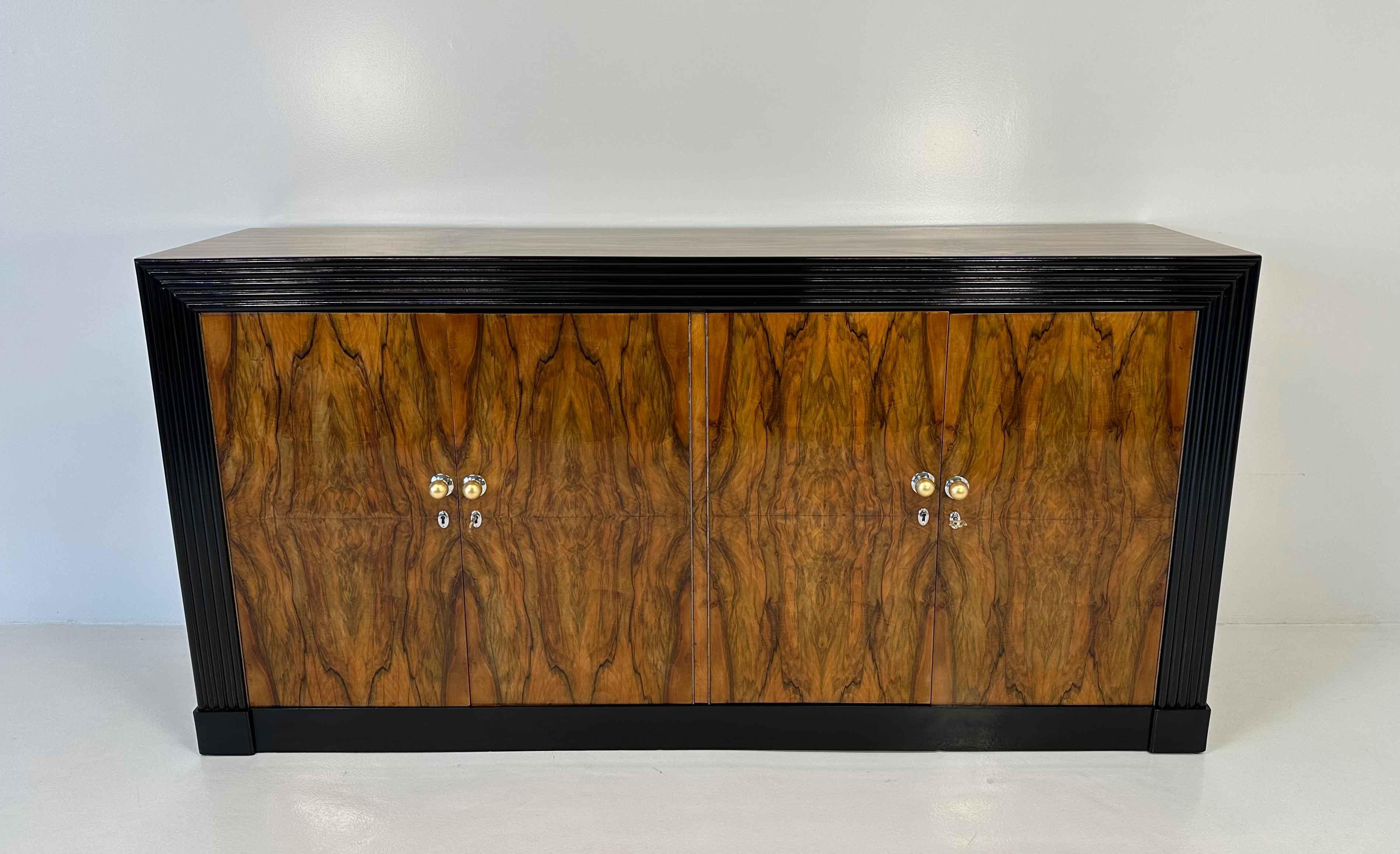 Dieses Art-Déco-Sideboard wurde in den 1930er Jahren in Italien hergestellt und ist im Stil von Gio Ponti gehalten. 
Er ist mit einem eleganten Nussbaumholz verkleidet, das von einem geriffelten, schwarz lackierten Holzprofil eingerahmt wird. 
Die