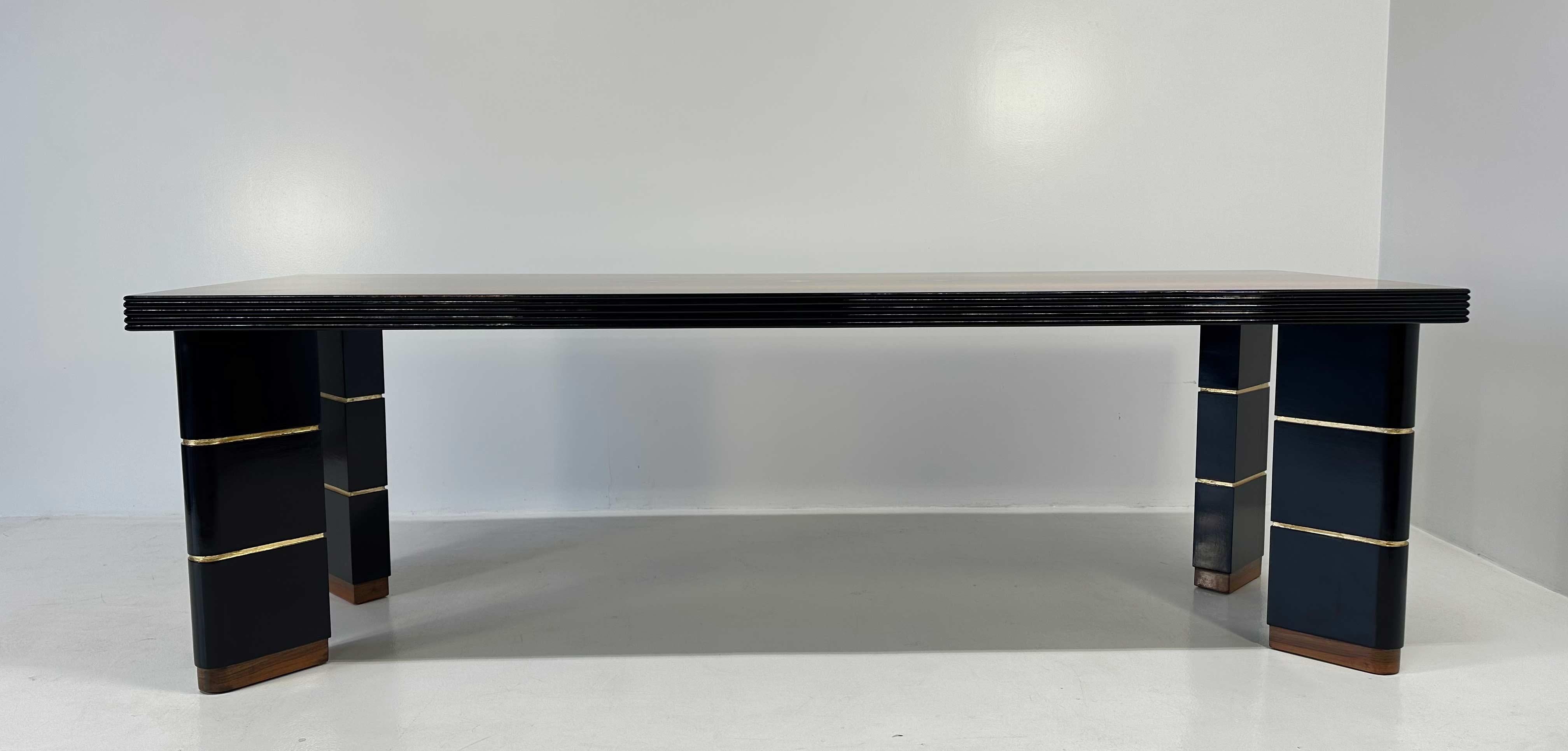 Dieser italienische Art-déco-Tisch aus den 1940er Jahren ist ein elegantes Beispiel für raffiniertes Design. 
Er ist aus Nussbaumholz gefertigt und verfügt über schwarz glänzend lackierte Beine und Profile, die durch goldene Blattgolddetails