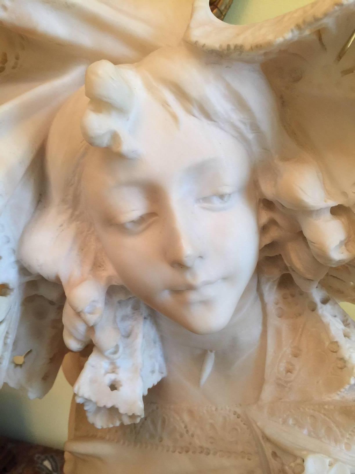 Exceptional hand carved Art Nouveau bust of a young woman. Her elaborate hat framing a beautiful face. The style clothing of the late 19th century Art Nouveau period. The bust rests on a round marble pedestal base.