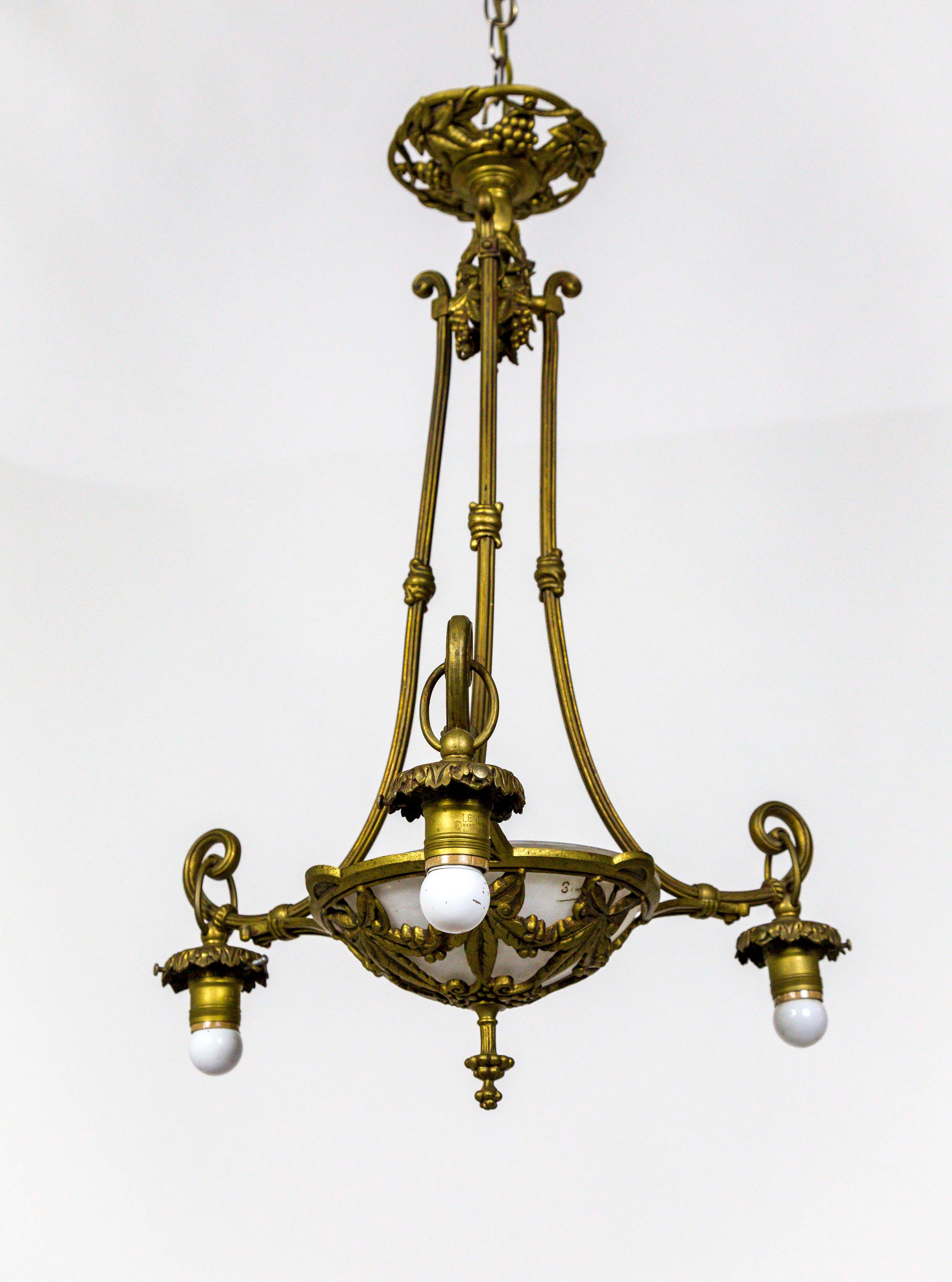 This 4-light, brass, Art Nouveau chandelier has 3 arms surrounding a circular, leaf and berry motif armature that holds a glass bowl. The design is echoed on the canopy and at the top of the stems. The fourth light is hidden and pointing down into