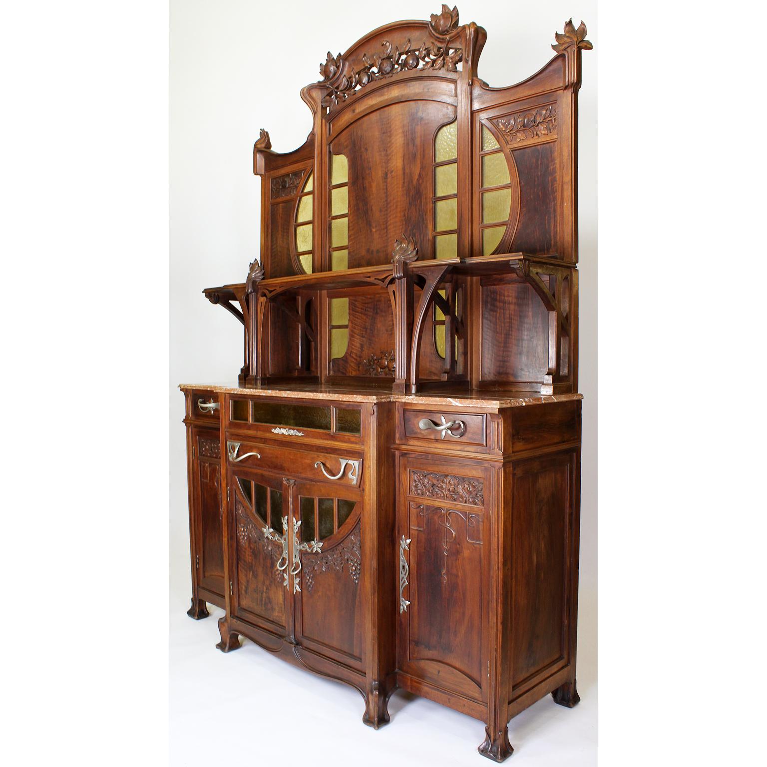 Una credenza buffet in noce intagliato di Vittorio Valabrega (1861-1952) del XIX-XX secolo. L'alto corpo in noce finemente intagliato con due ante centrali scolpite con tralci d'uva, dotate di pannelli in vetro giallo artigianale modellato sopra un