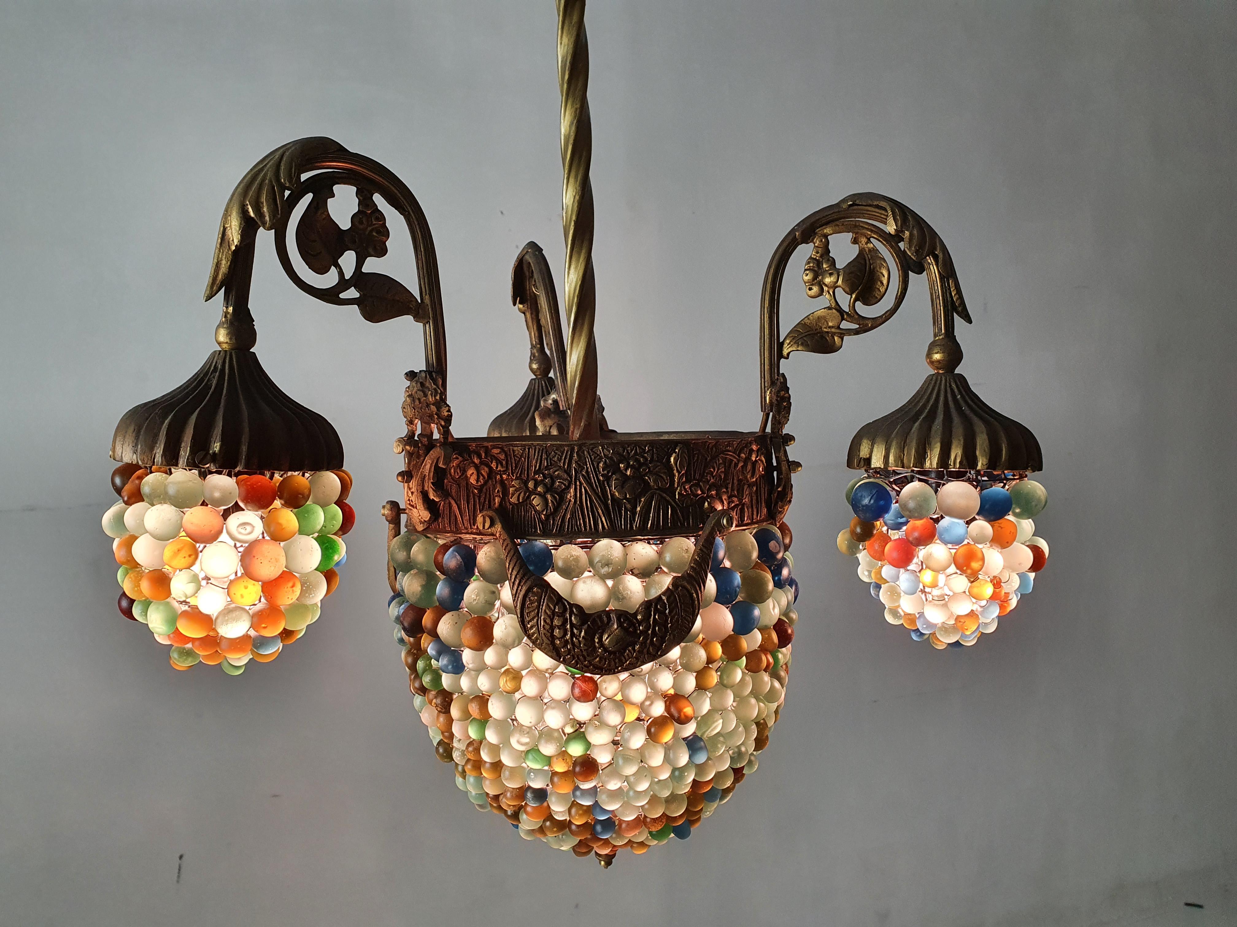A chandelier in Art Noveau style made with a structure in bronze and adorned with an array of different colored solid glass beads. The arms and centre has a decor of different flowers and leaves and the lampshades are of handmade glass beads. The