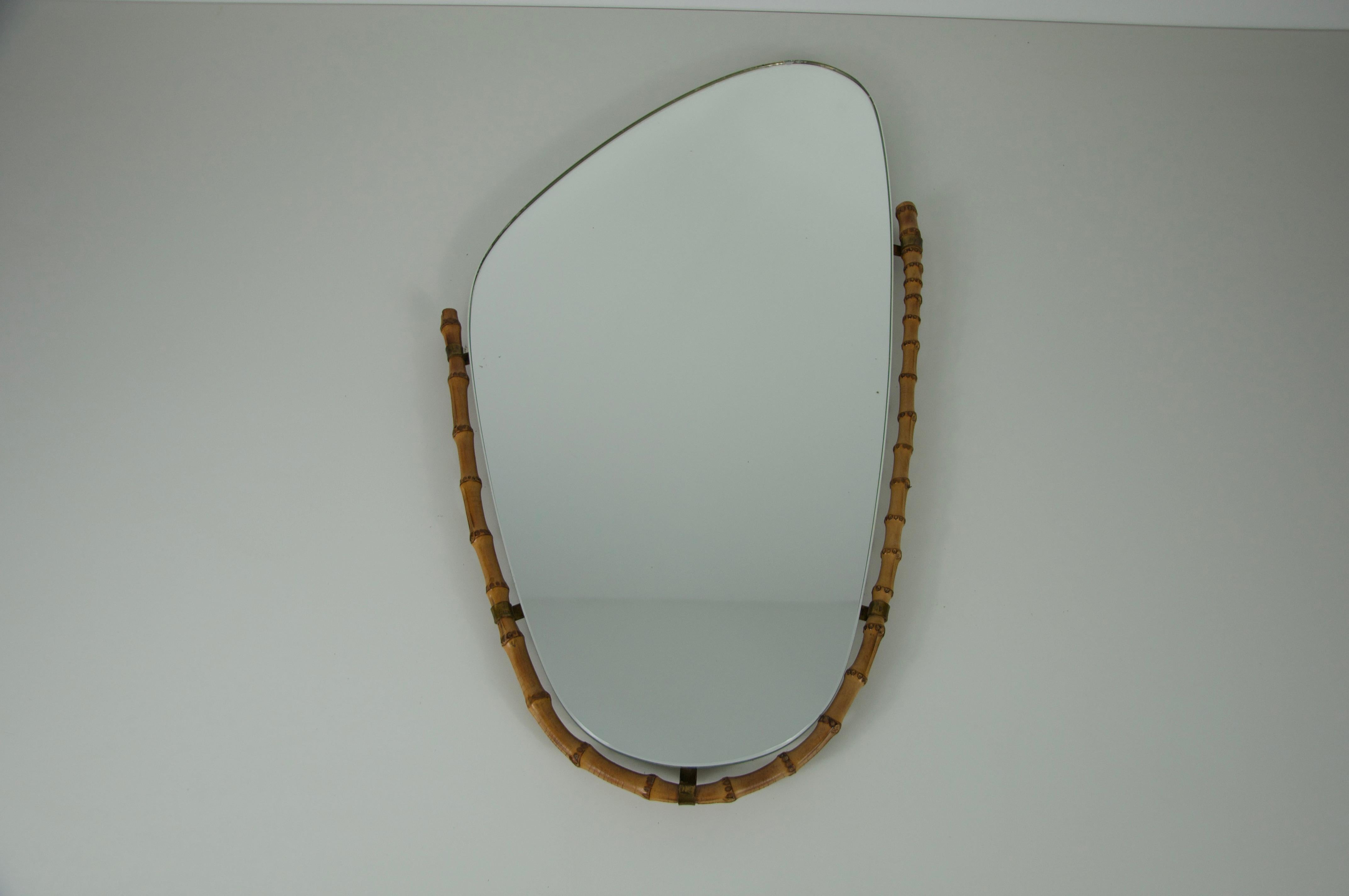 Cet exquis miroir italien des années 1960 est un parfait exemple de l'artisanat du milieu du siècle, combinant des matériaux organiques avec un design raffiné et asymétrique. Le verre miroir de forme unique est accentué par un cadre en bambou et en