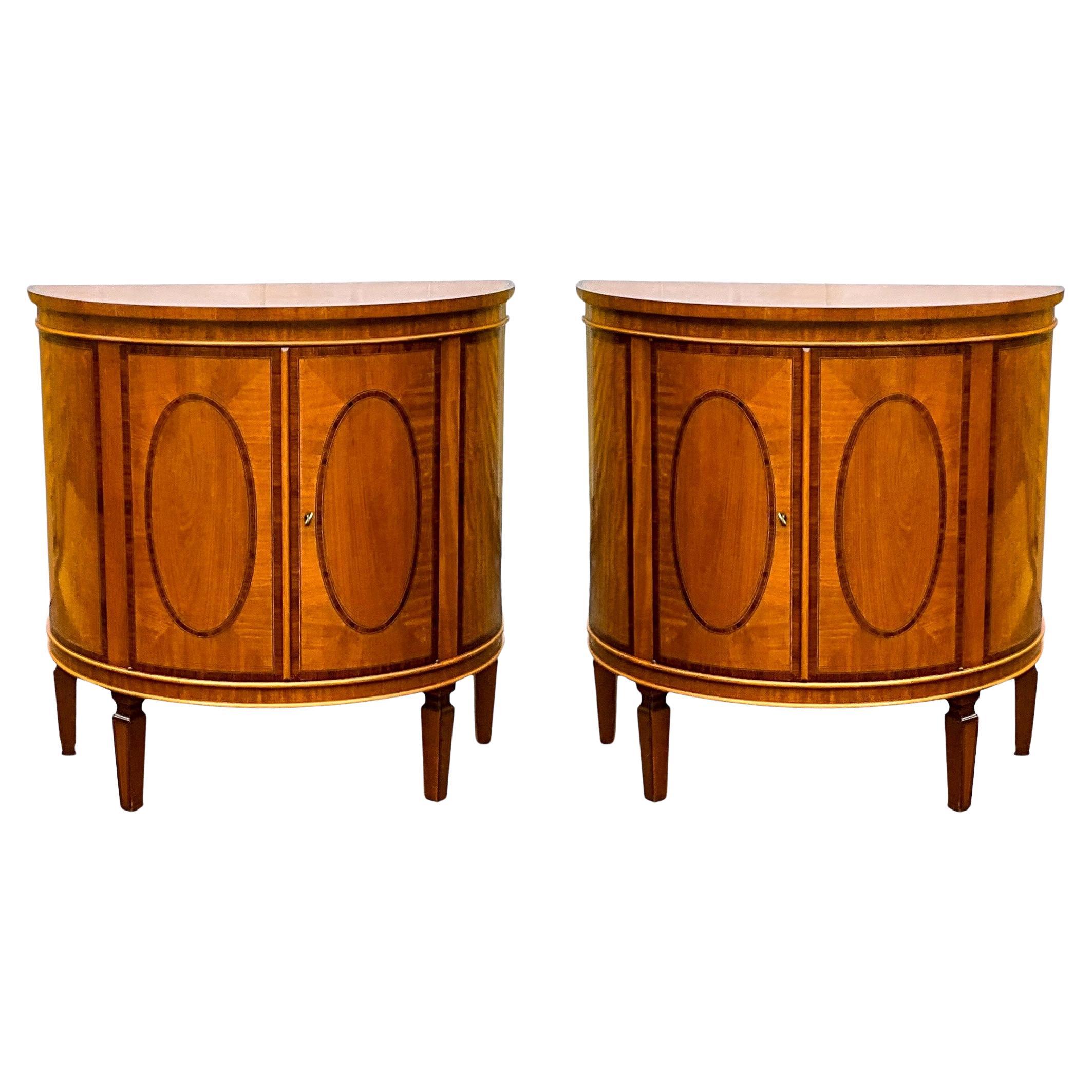 This is a lovely pair of Italian inlaid and banded satinwood demilune cabinets attributed to Decorative Crafts. They are in very good condition with each having a single interior shelf and key. They pair are not marked and date to the later part of