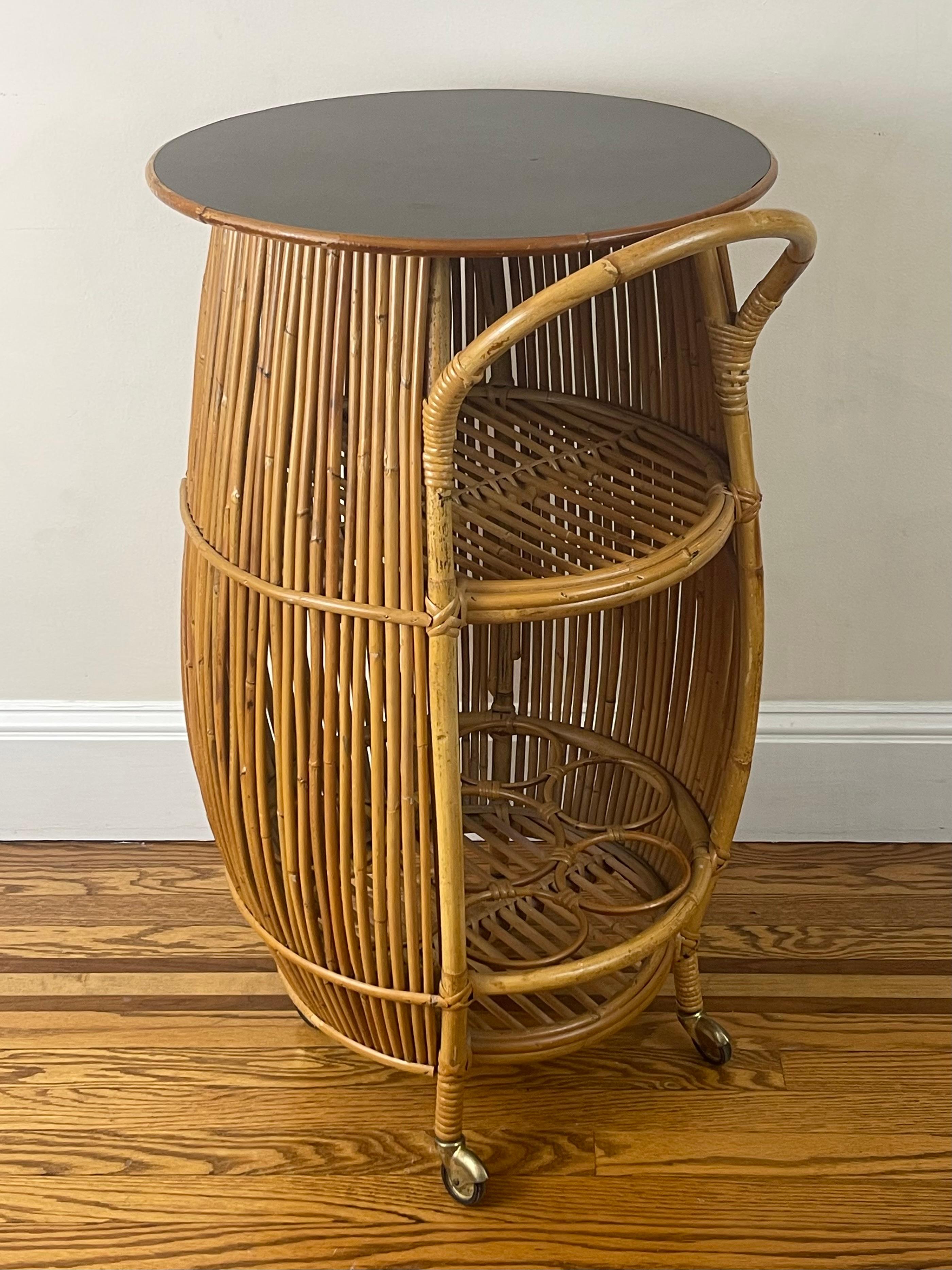 Splendid barrel-shaped bar cart in bamboo and rattan manufactured by Bonacina, Italy, c. 1960s. With its interior shelf, bottle rack, and black laminate top, this mid-century piece is as every bit as functional as it is decorative. Original brass