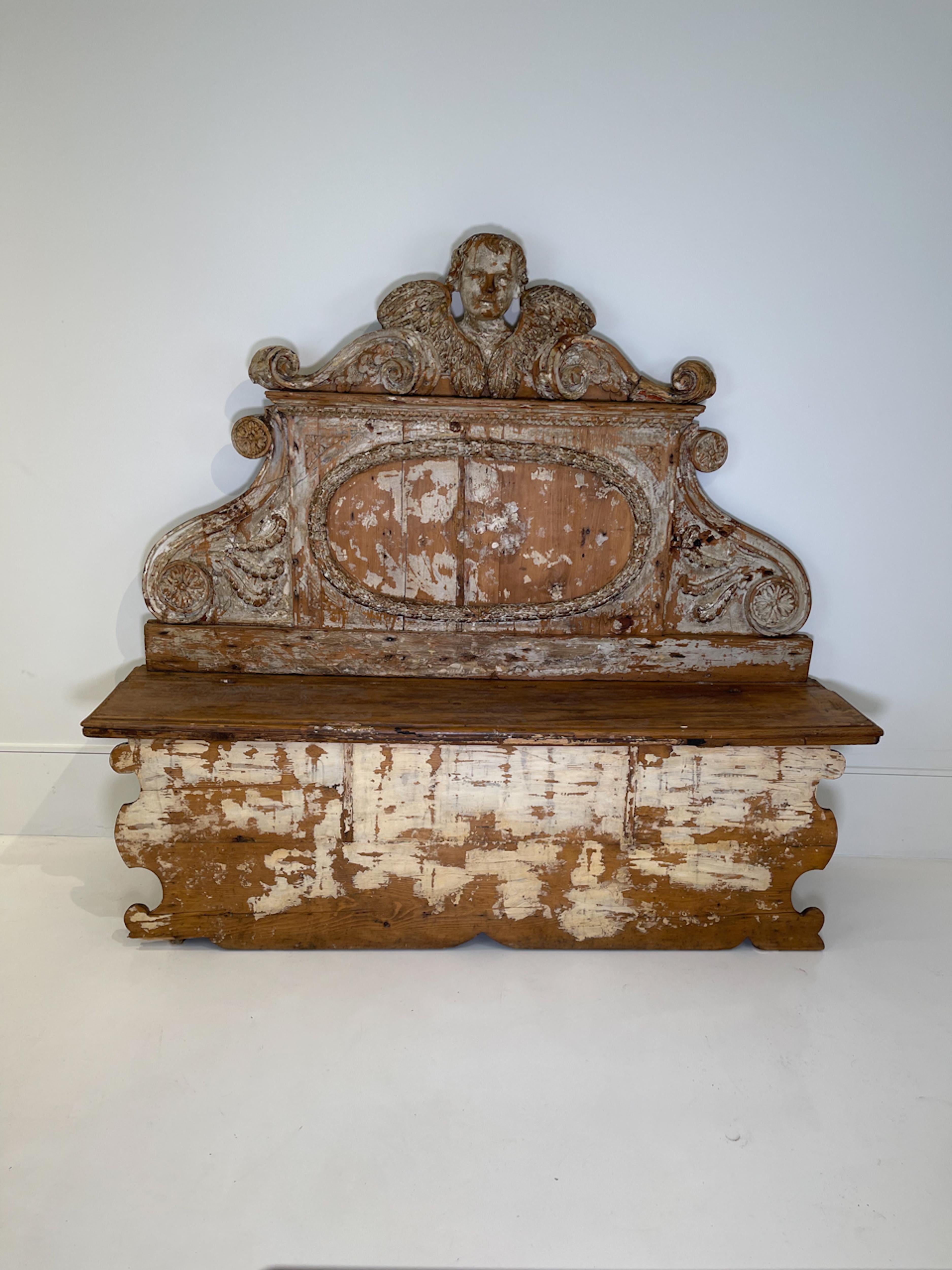 18th Century Italian wooden bench. Unique large scale wooden bench with beautifully carved details of an angel's face and wings, as well as scrollwork, florets and acanthus leaves. Was likely used in an entry hall for seating and storage and would