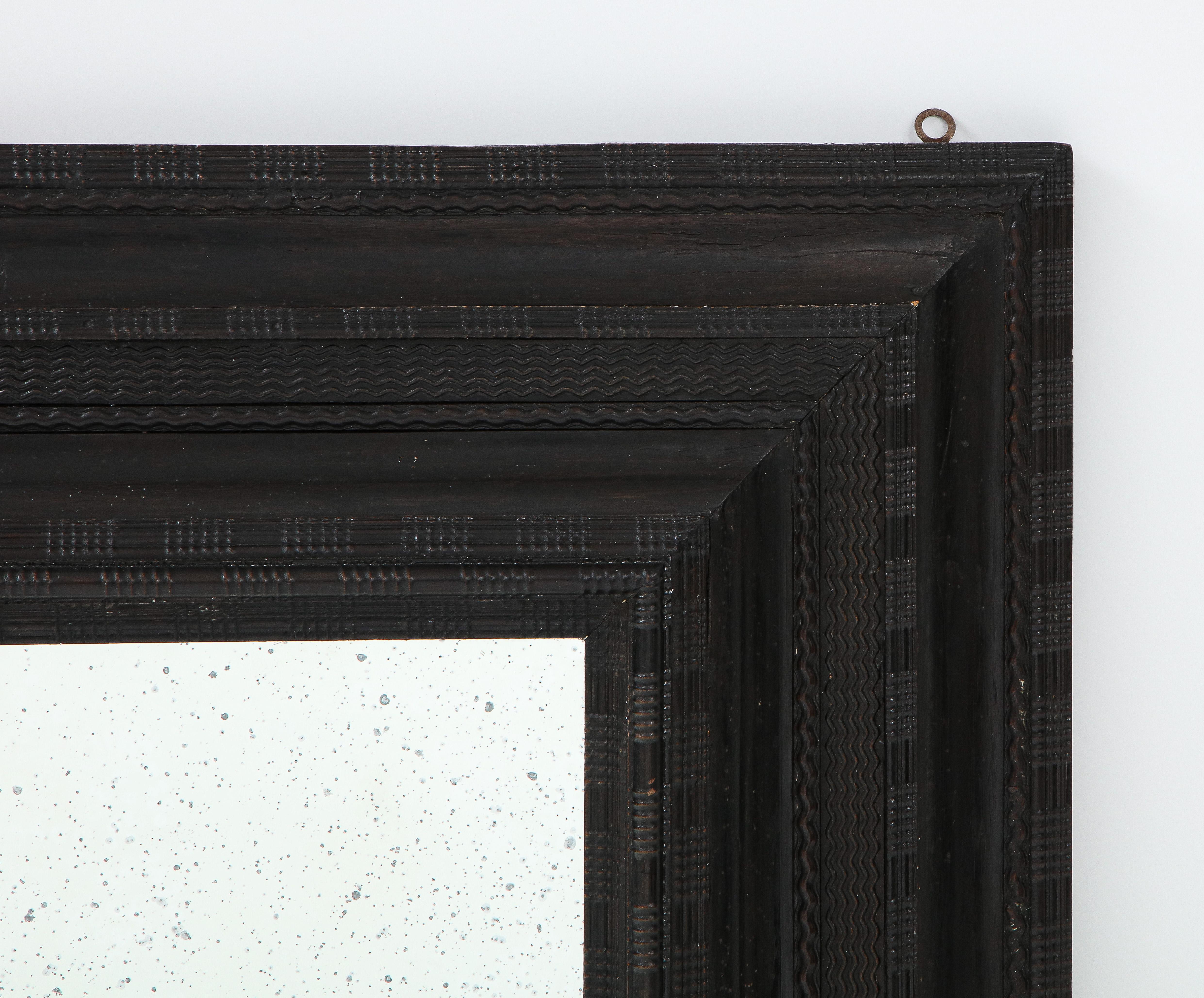 An exceptional Northern Italian Baroque intricately carved ebonized frame, inset with antiqued glass. The frame with cove carved 'ripple' molding and its original forged iron hooks on the back. These style of frames are usually referred to as Dutch,