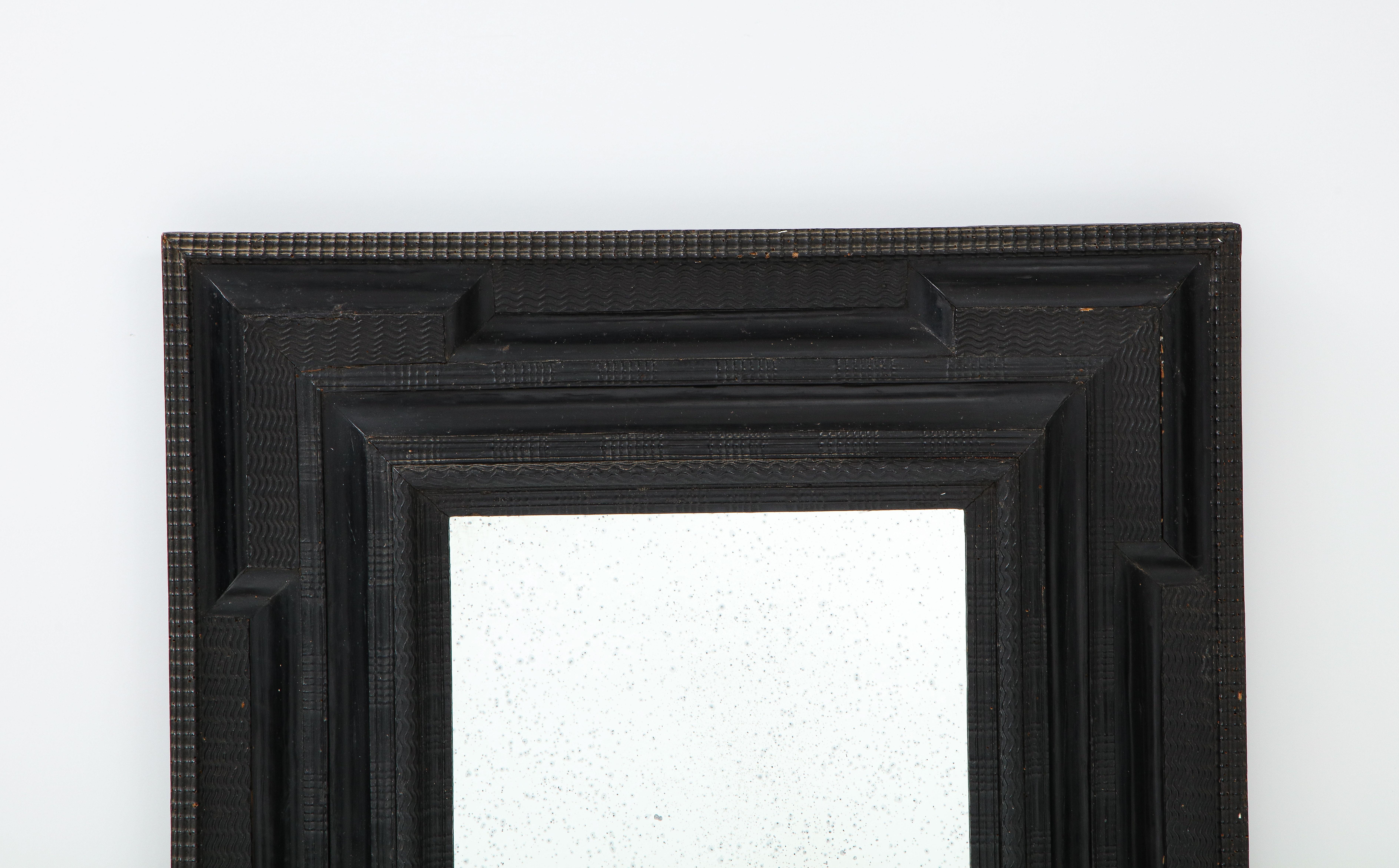 An exceptional Northern Italian Baroque intricately carved ebonized frame, inset with antiqued mirror glass. The frame with cove carved 'ripple' molding and its original forged iron hook on the back. These style of frames are usually referred to as