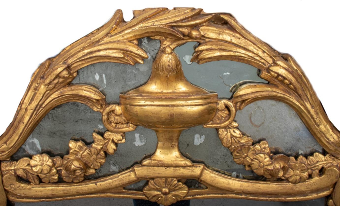 Italian Baroque wall mirror in carved gilt wood with swags and volutes and centered tympanum urn flanked by fruit garlands, 18th century or later. 44
