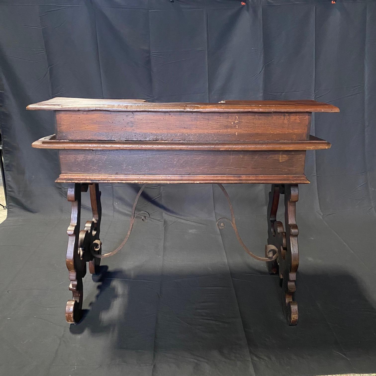 An Italian Baroque style walnut writing desk table with drawers and lyre shaped base legs and beautiful hand crafted wrought-iron stretchers. Created in Italy during the early years of the 19th century, this walnut writing desk or table features a