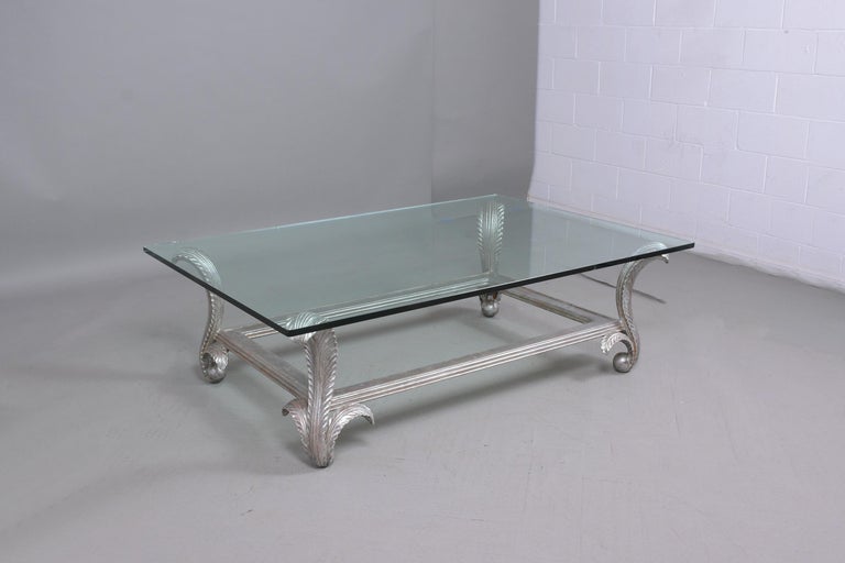 A 1970s vintage coffee table hand-crafted out of wood has been restored and is in great condition, this fabulous cocktail table features a silver-leaf finish rectangular clear glass top in good condition supported by four sturdy scroll carved legs