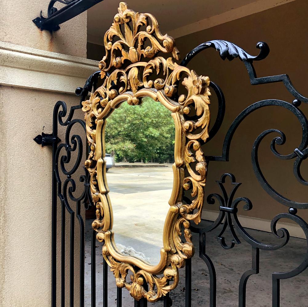 Italian Baroque giltwood mirror was hand-carved from solid wood in an elaborate design which features full sculpting allowing the wall to show through the pierced openings in the design. Foliate motifs dominate the composition, creating a shield or