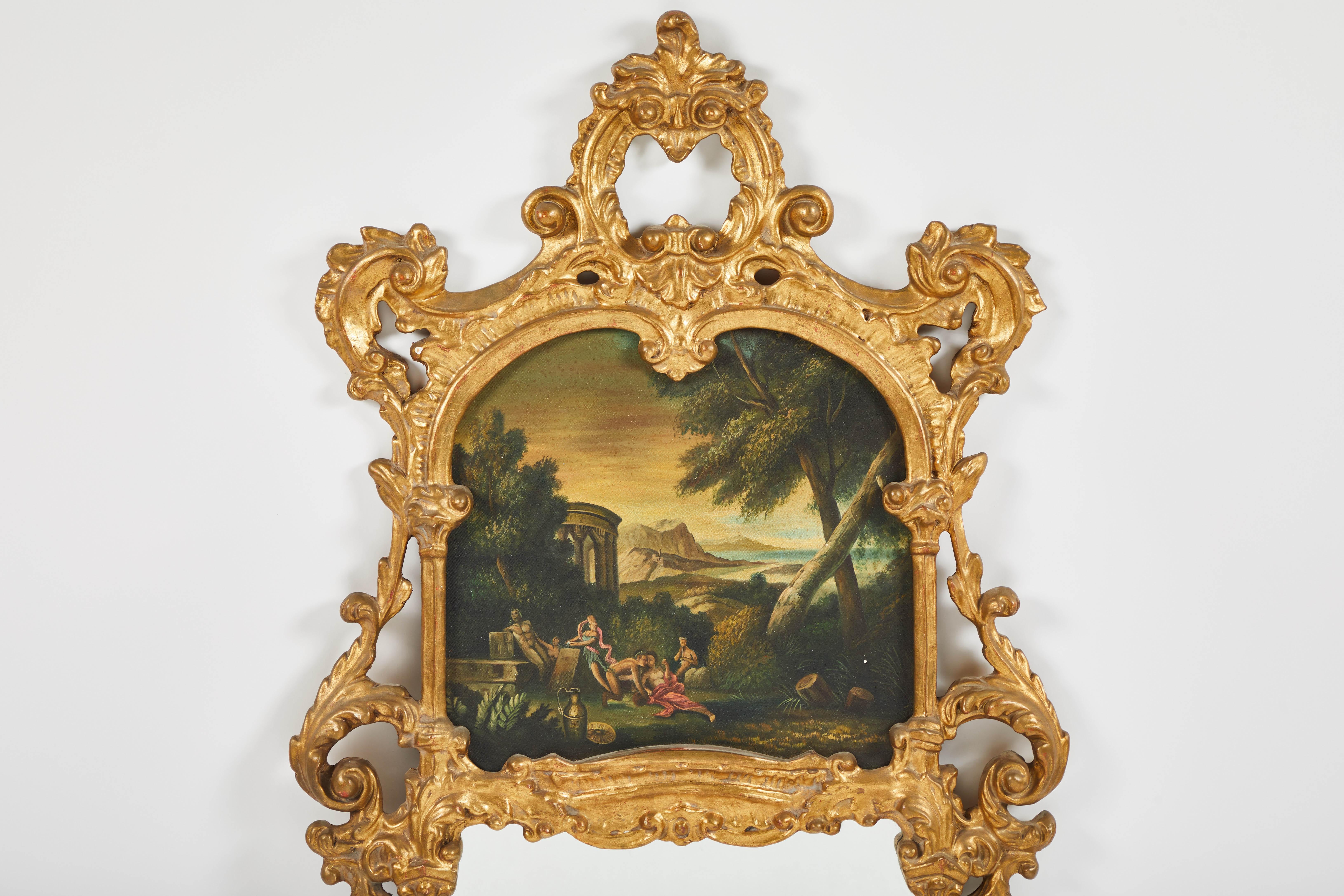 An Italian Baroque mirror style carved giltwood trumeau mirror. The painting depicts a lunching party in a forest with ruins in the background, 19th century.


