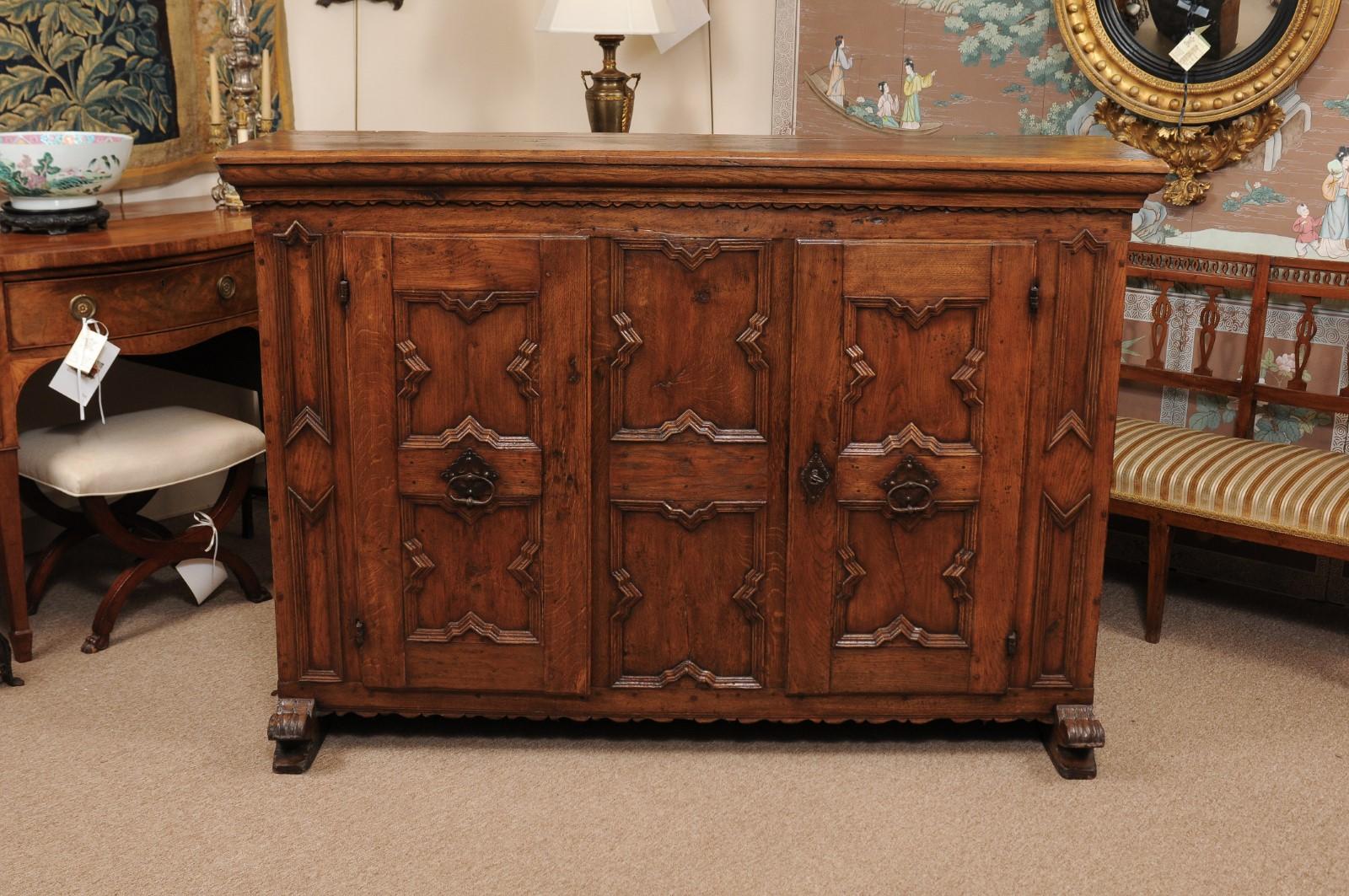 The Italian early 18th century baroque tall oak credenza with rectangular top, the front with molded geometric design and 2 cabinet paneled doors ending in carved feet.