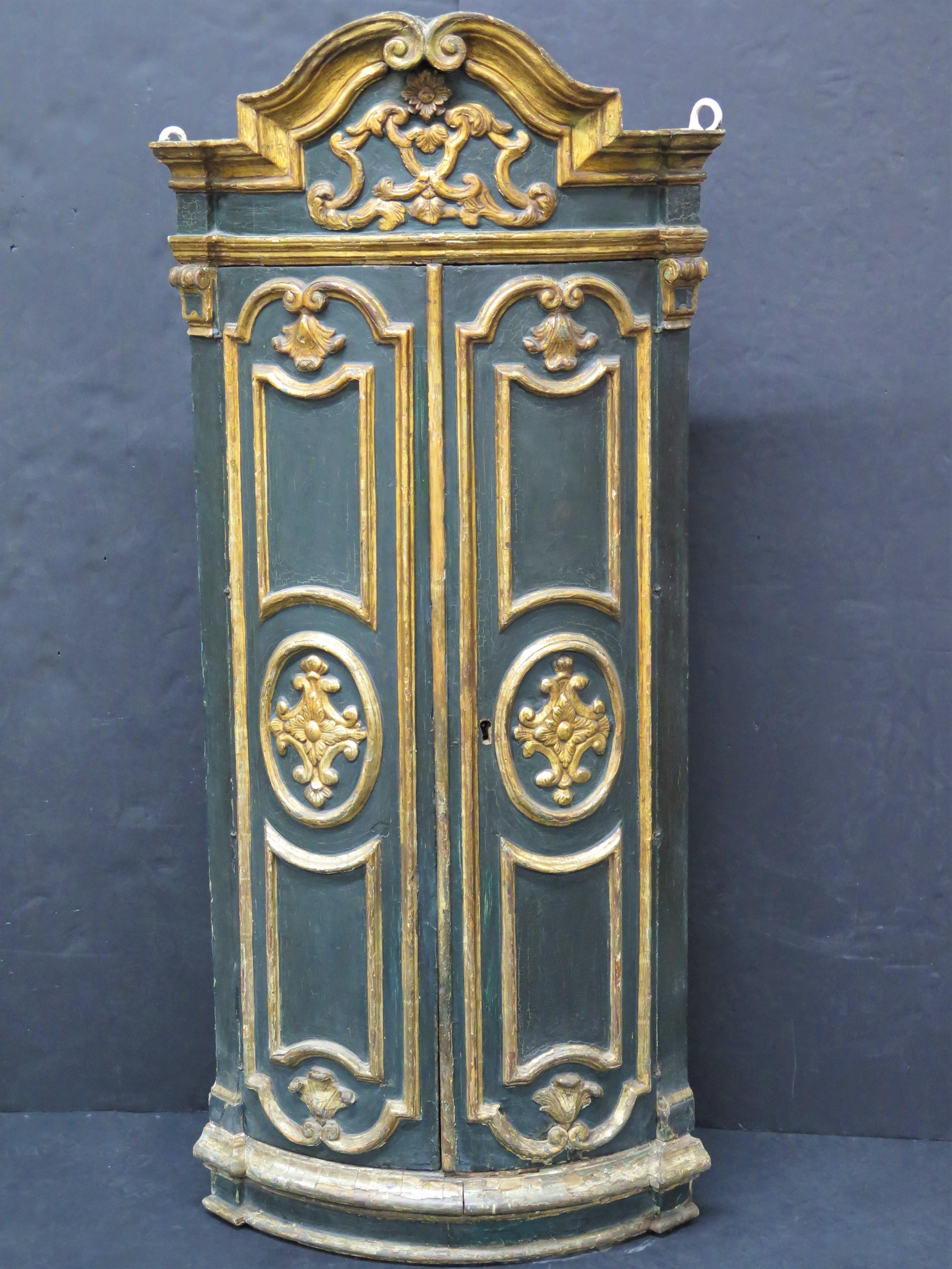 Armario esquinero italiano barroco pintado de verde y dorado con puertas de cuarterones, pieza de bella forma, interior y estantes forrados con papel pintado antiguo, del siglo XIX, de color marrón, con un dibujo cubierto de pequeñas estrellas y
