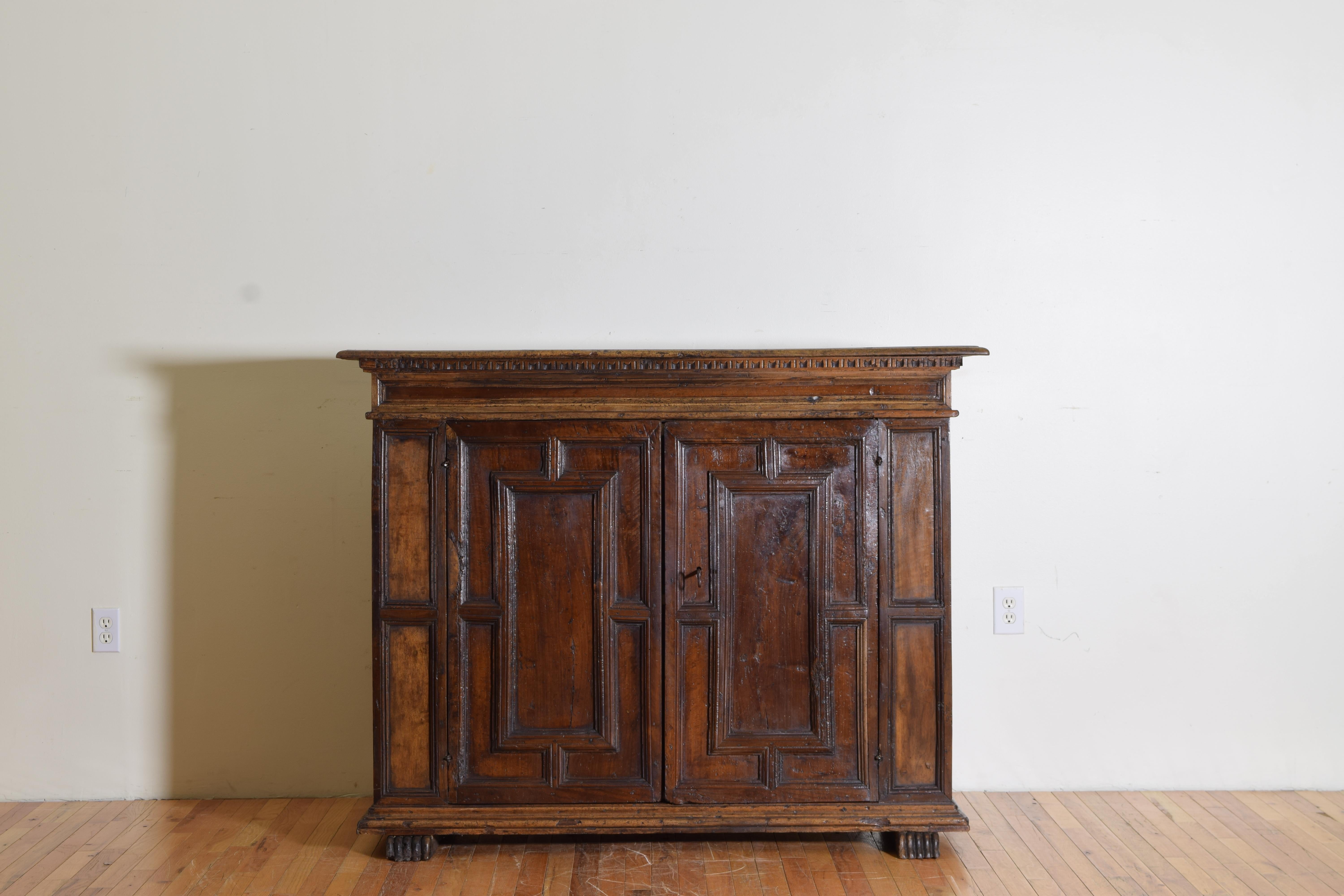 having a rectangular top with dentile molded edge above a conforming case, the doors with raised panels and opening to reveal interior shelving, raised on carved paw feet, depth of 20